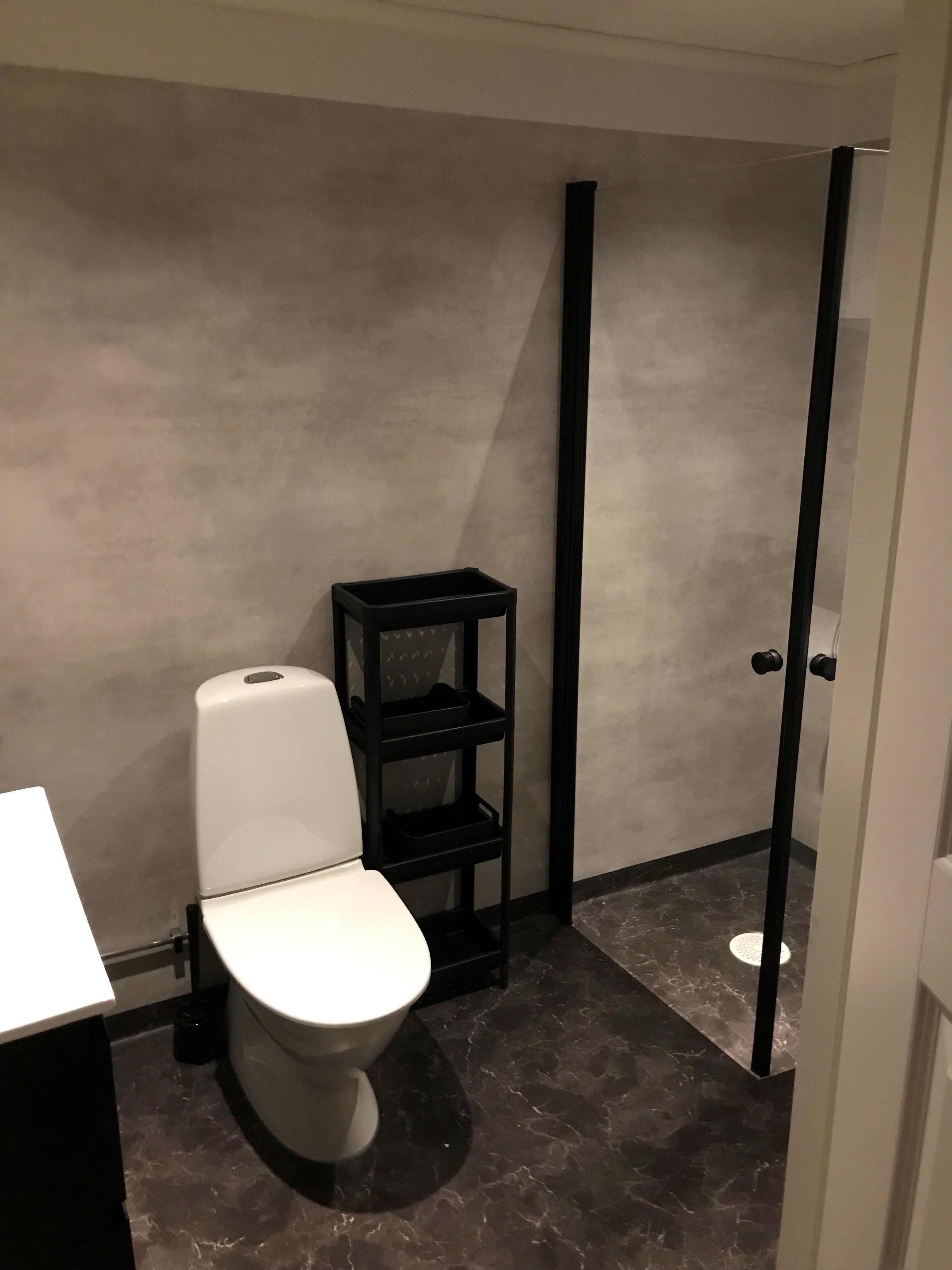 Nyrenoverat badrum. Vit toalett och dusch med svarta detaljer.