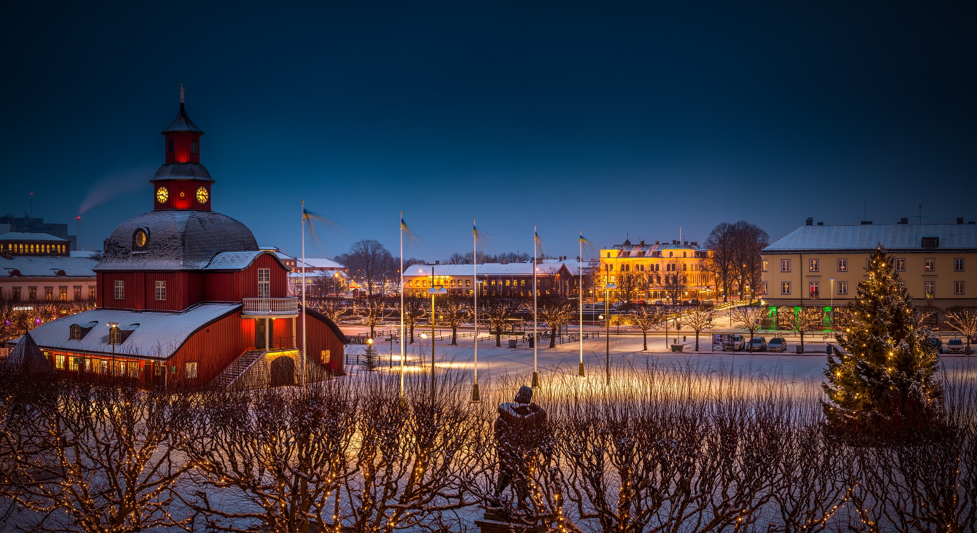 Ett rött stort trähus på ett torg med träd runt torget.