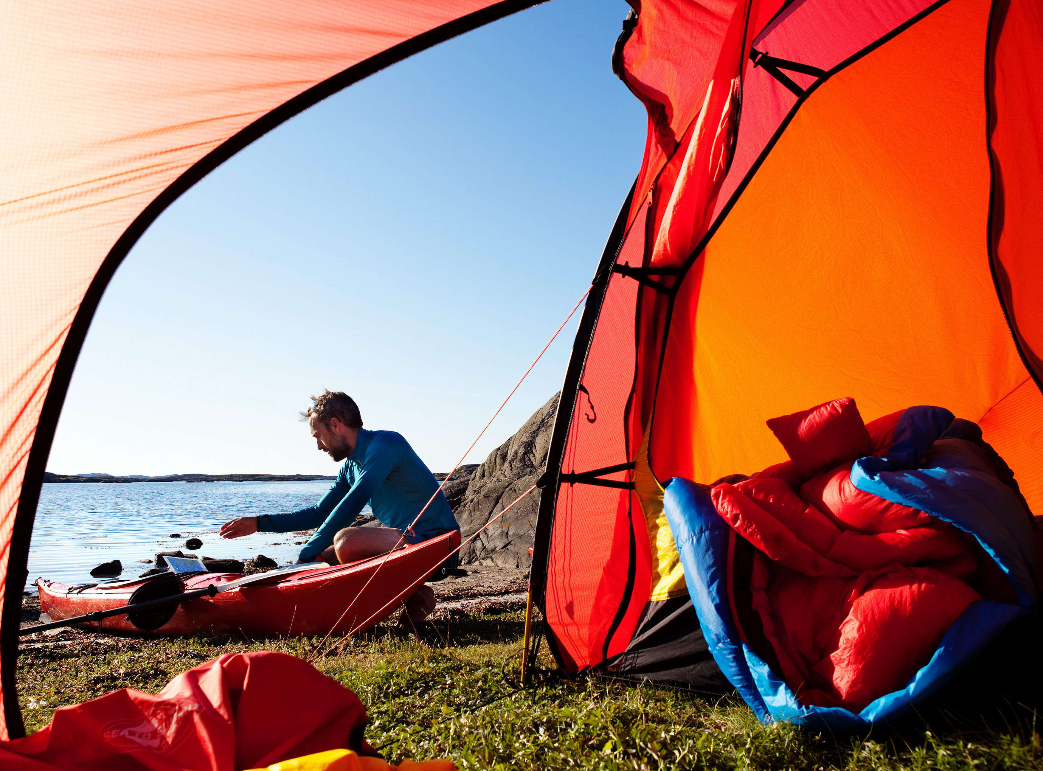 En man sitter utanför sitt tält och ordnar med sin kajak.