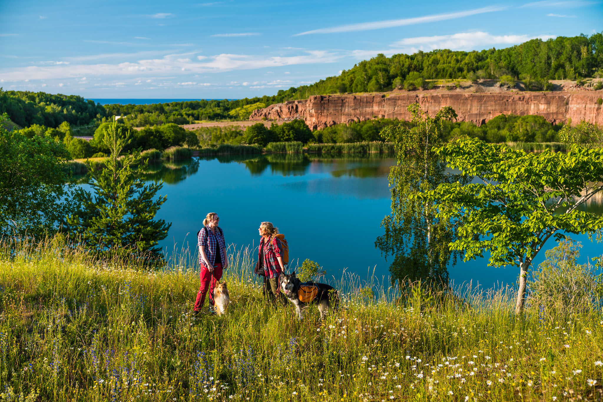 Två personer står vid kanten av ett vattenfyllt stenbrott med sina hundar.