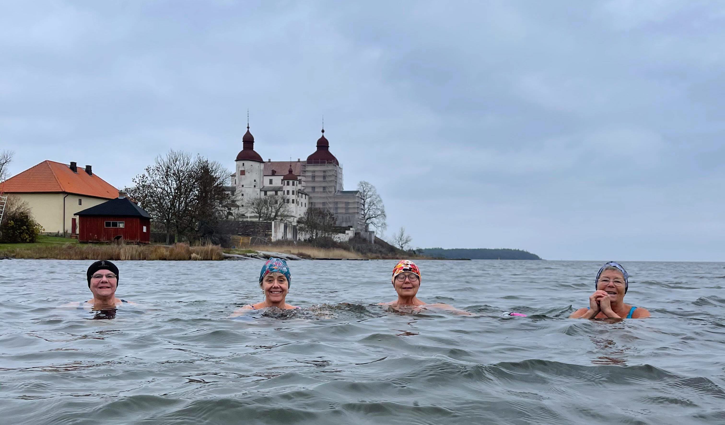 Fyra glada kvinnor som vinterbadar vid Läckö Slott. I bakgrunden skymtar slottet.