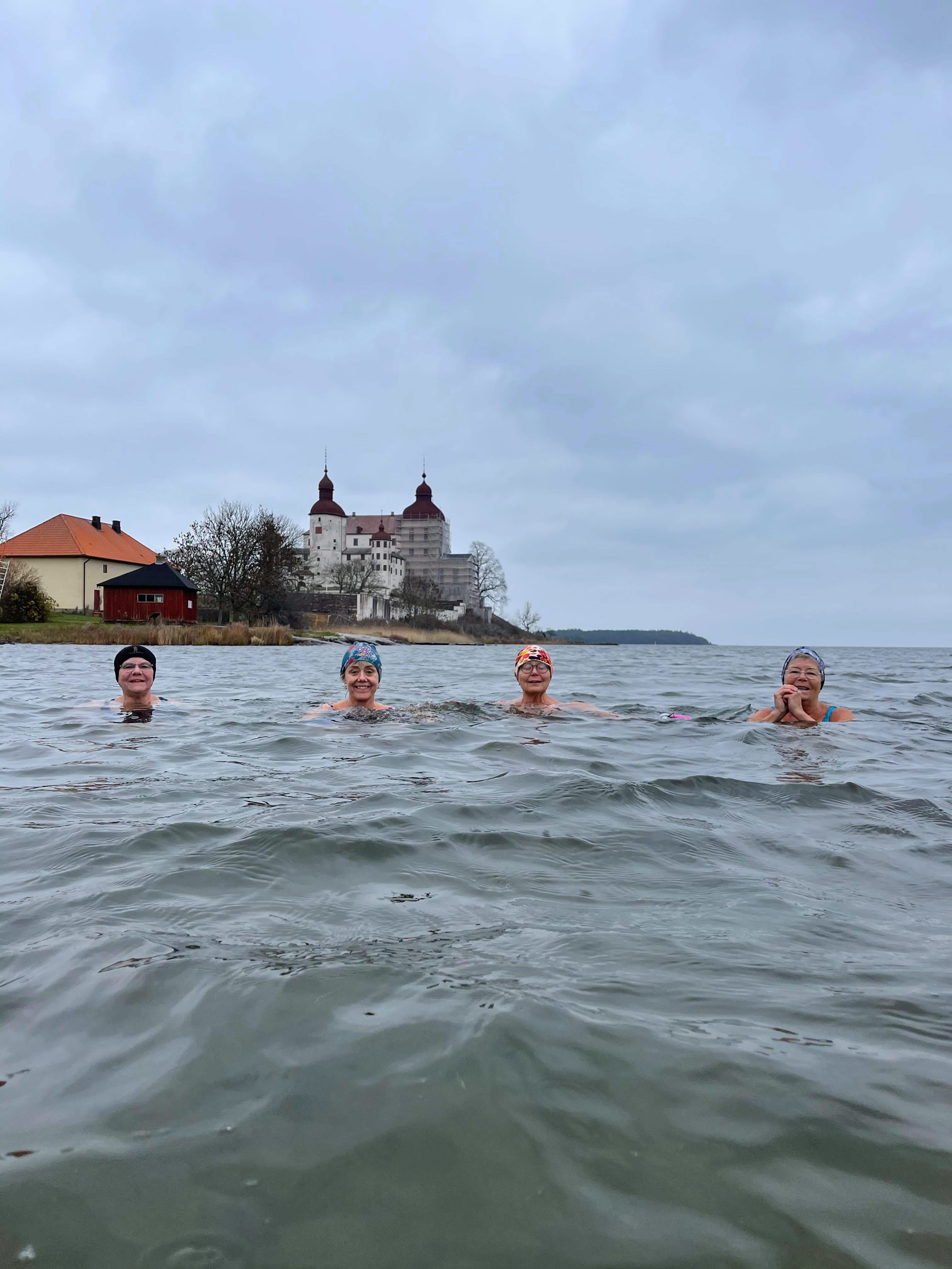 Fyra glada kvinnor som vinterbadar vid Läckö Slott. I bakgrunden skymtar slottet.