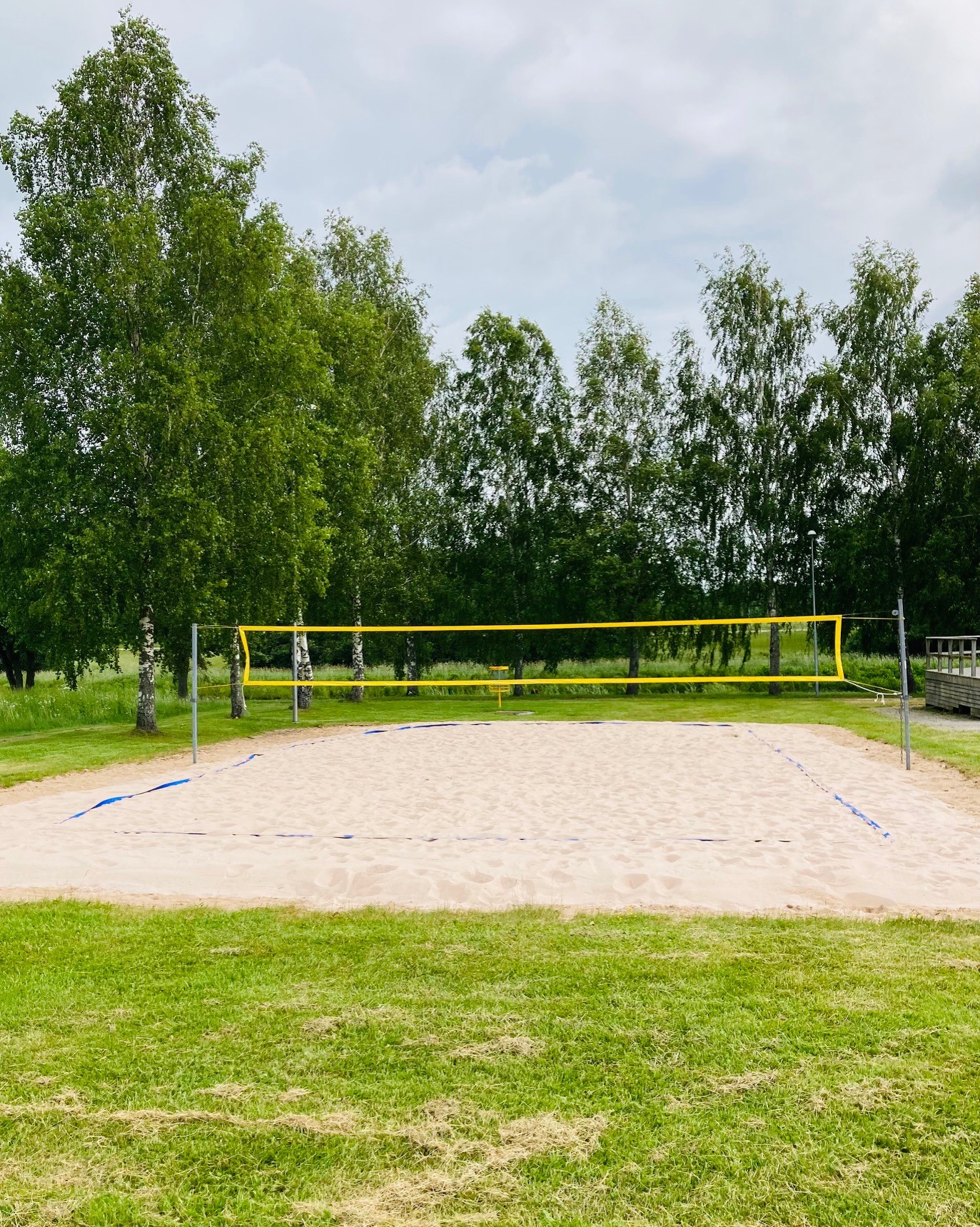 En volleybollplan med ett gult nät, sand på planen. Träd i bakgrunden. 