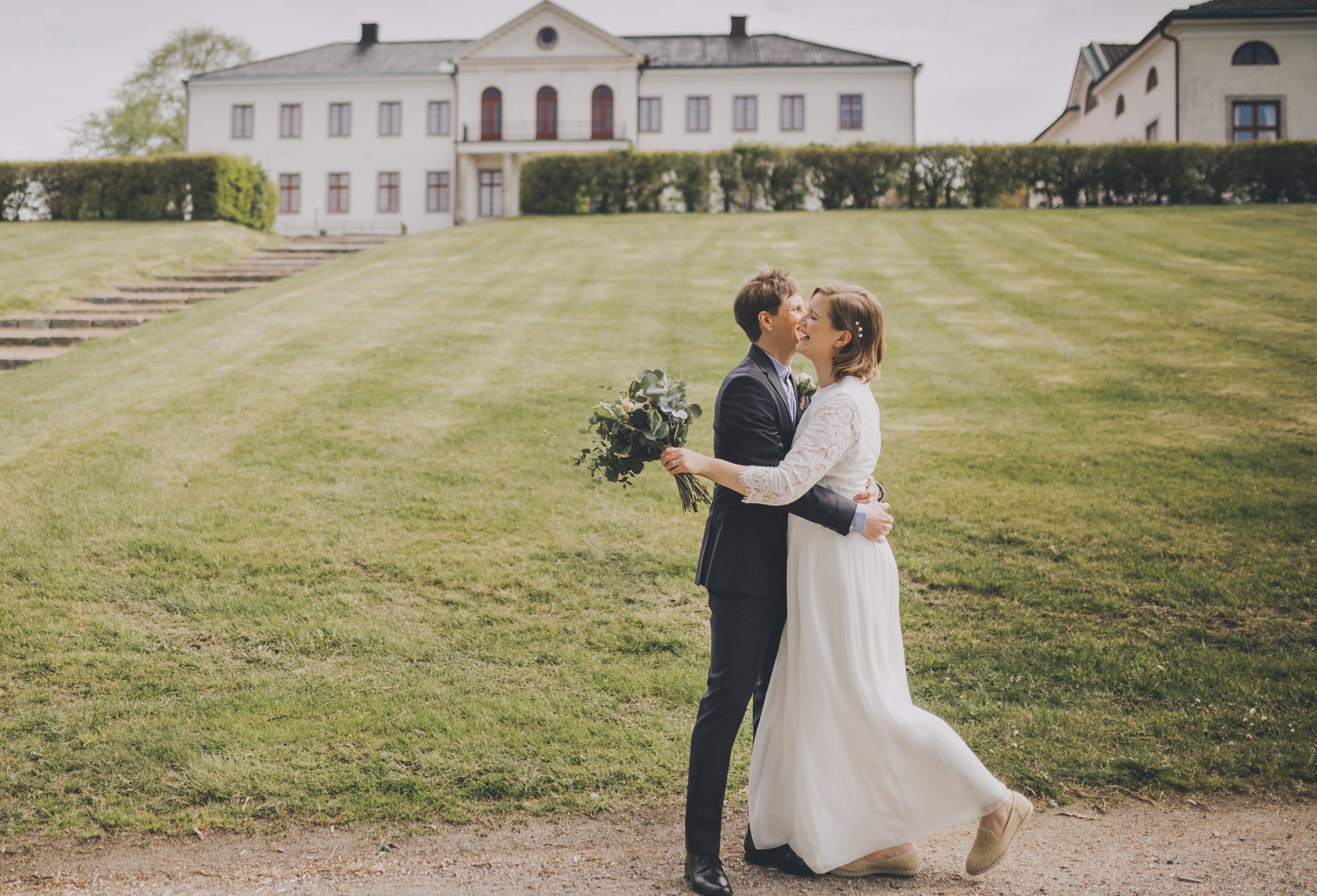 Ett brudpar omfamnar varandra i glädje framför Nääs Slott