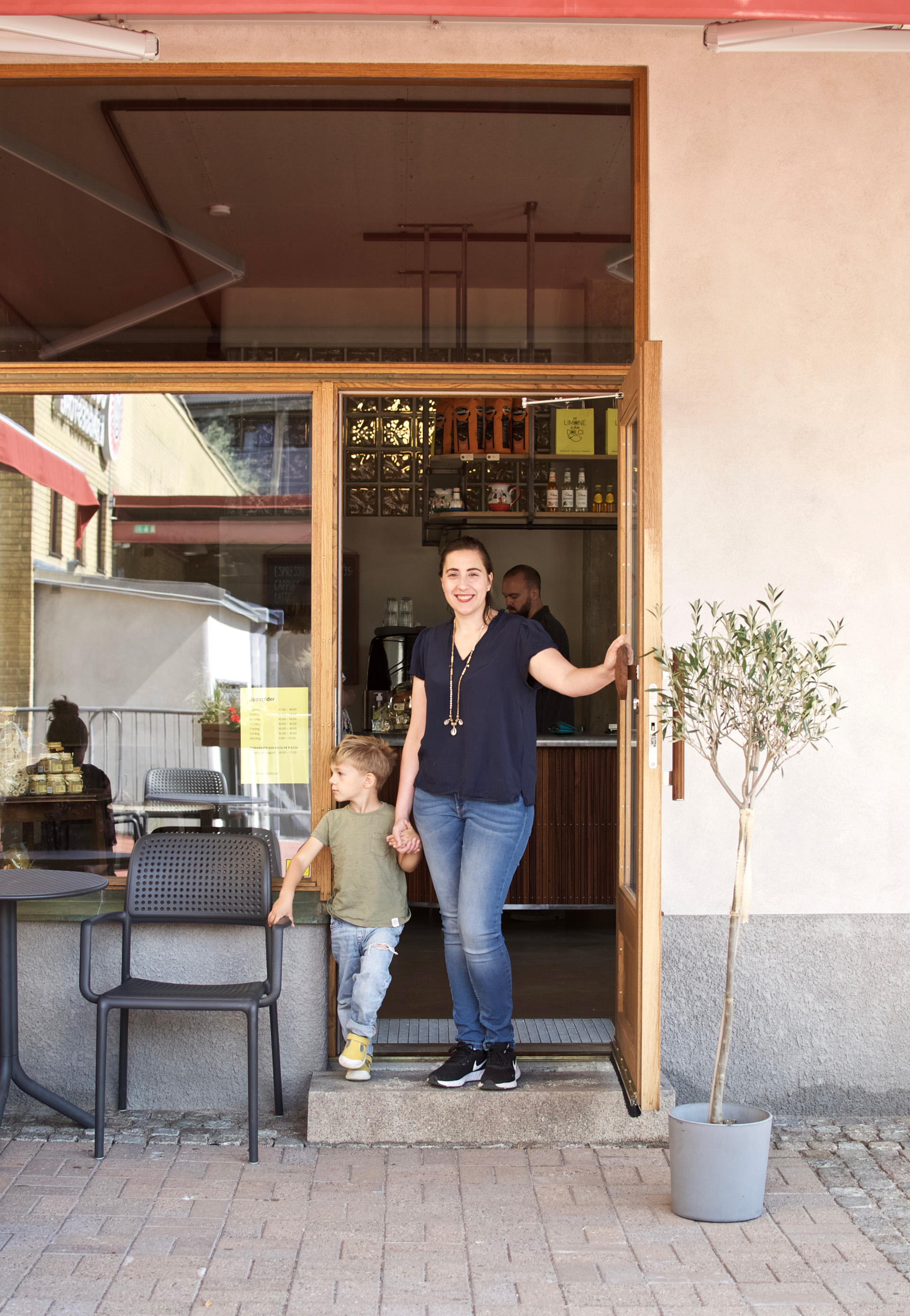 mamma med son vid glasdörr med olivträd 