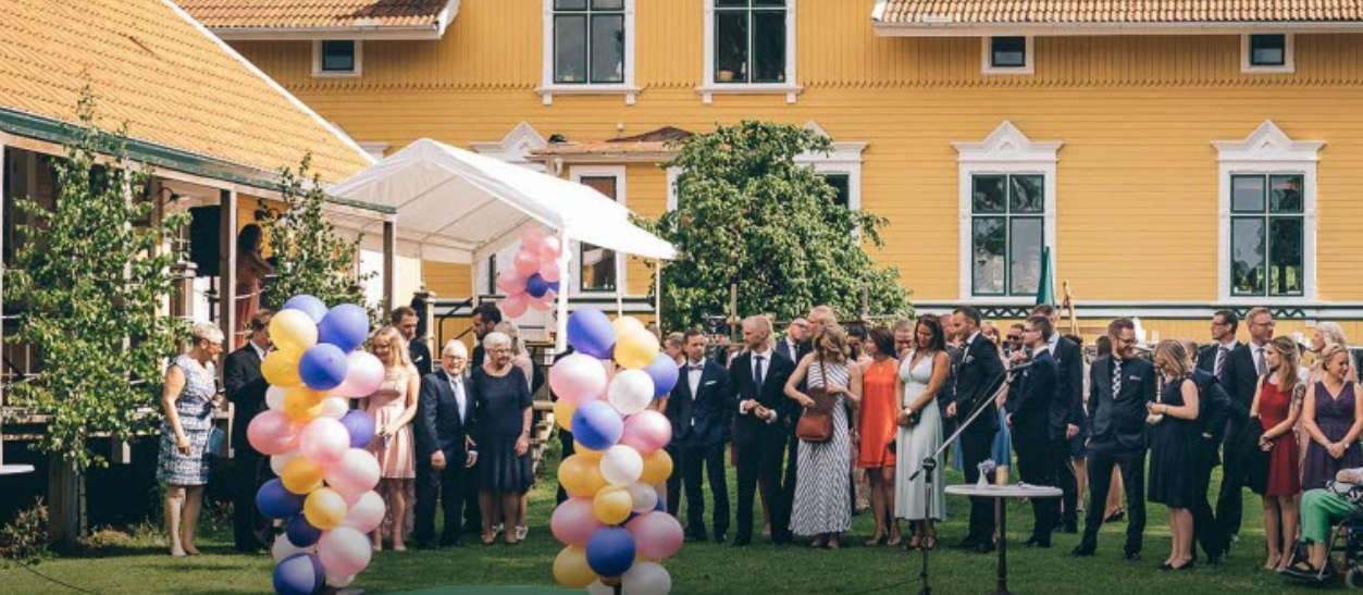 personer på fest/bröllop utomhus med gul villa i bakgrunden.