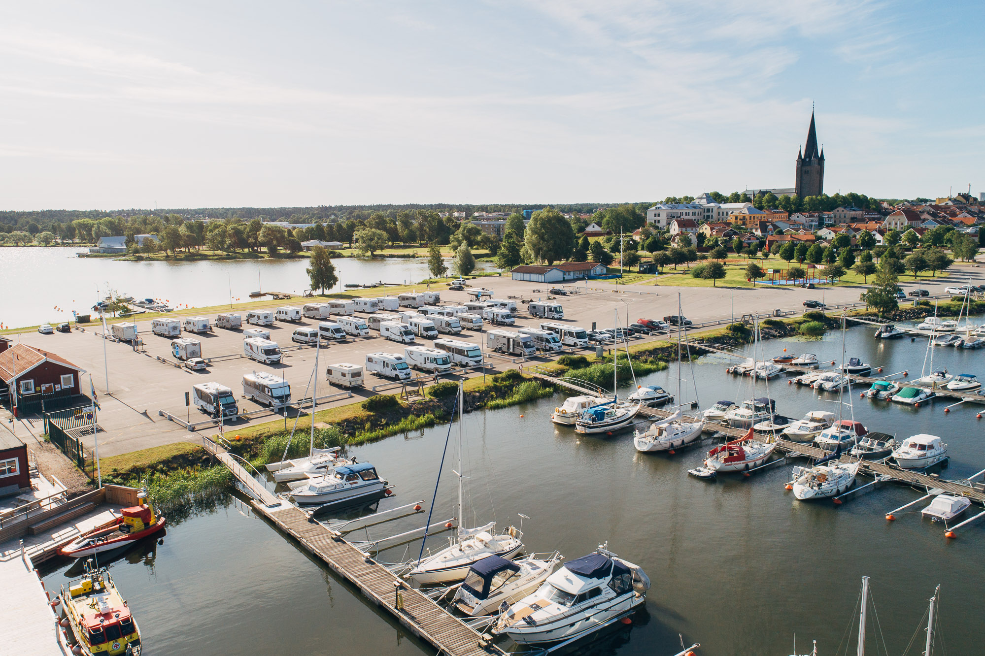 Flygbild över yttre hamnen i Mariestad, med husbilar på ställplatsen. Gamla Stan med domkyrkan i bakgrunden.
