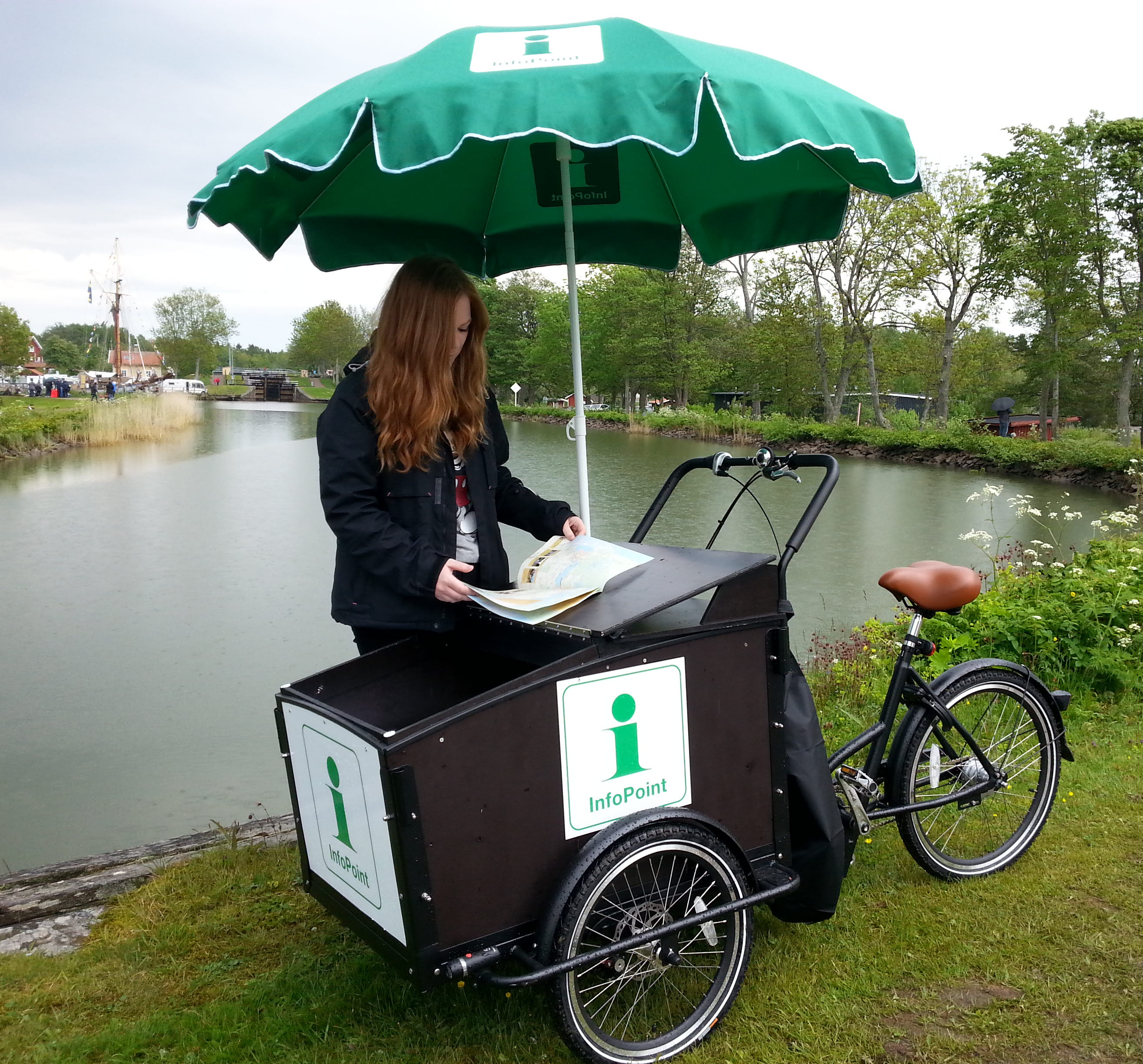 En person står och bläddrar i en broschyr vid en lådcykel. I bakgrunden synd Göta kanal.