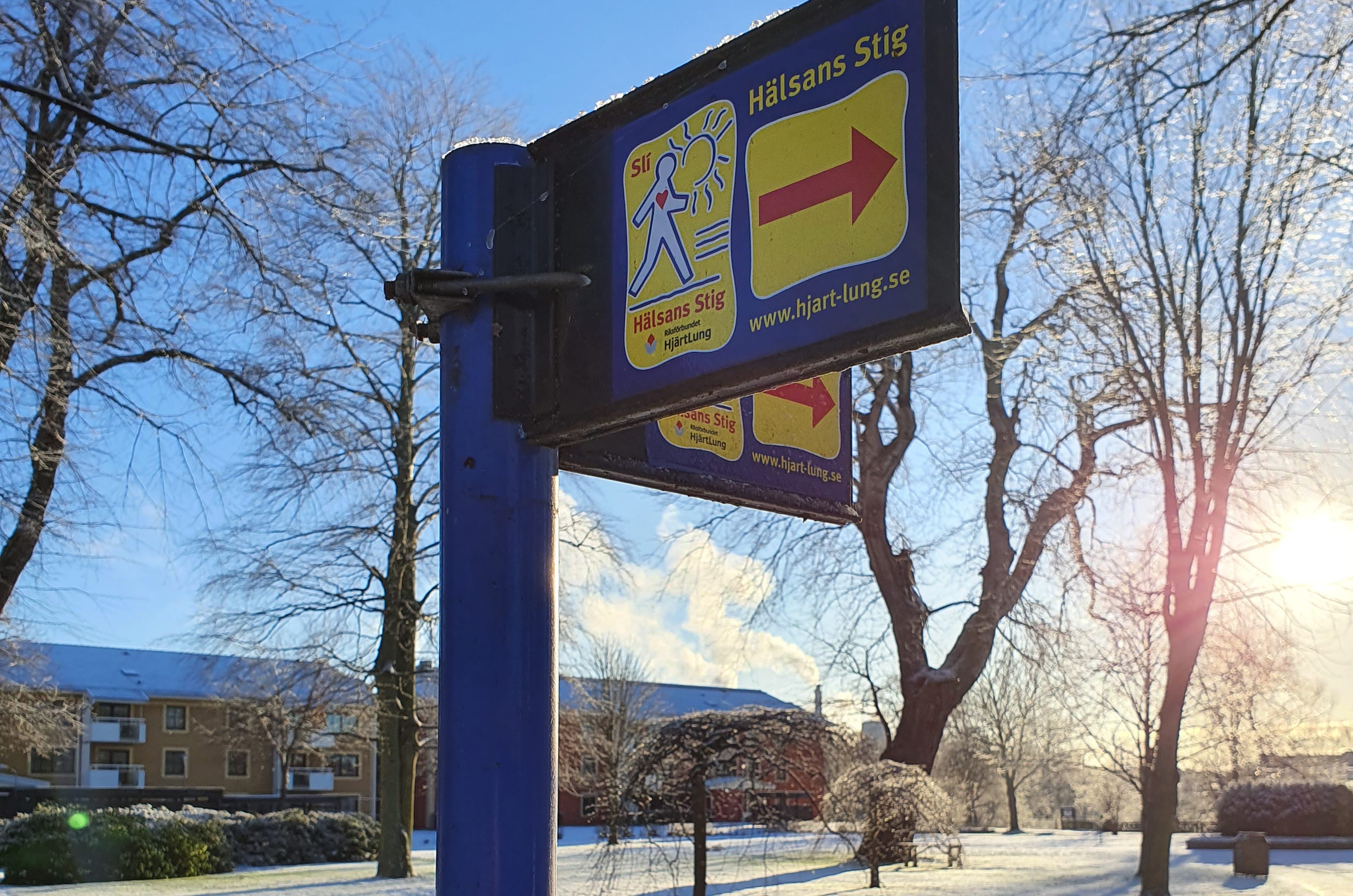 Skylt för Hälsans stig i Mariestad, vinterlandskap i bakgrunden.
