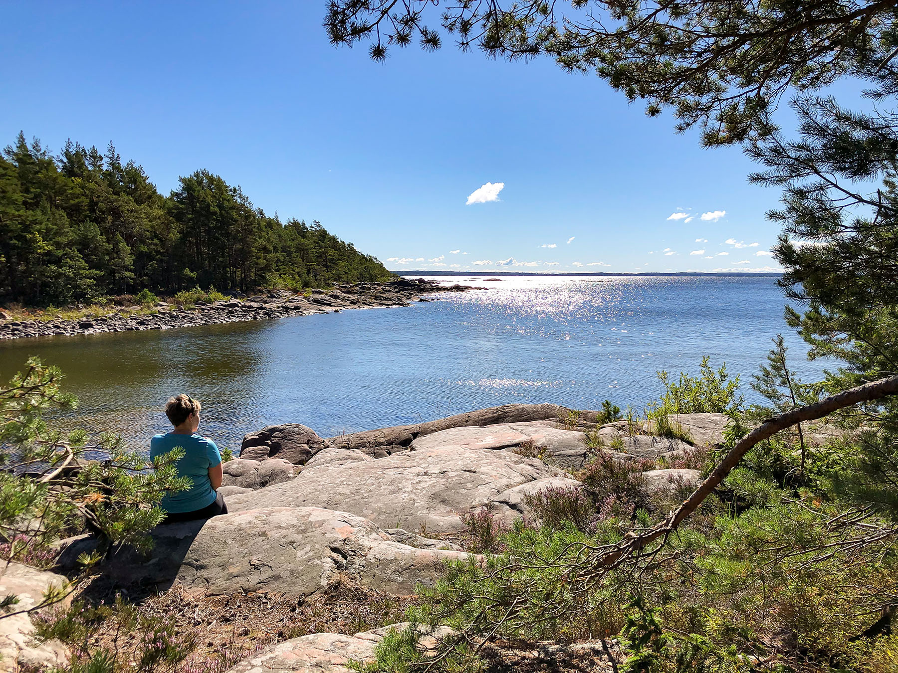 En kvinna sitter på en klippa och tittar ut över Vänerns vatten.