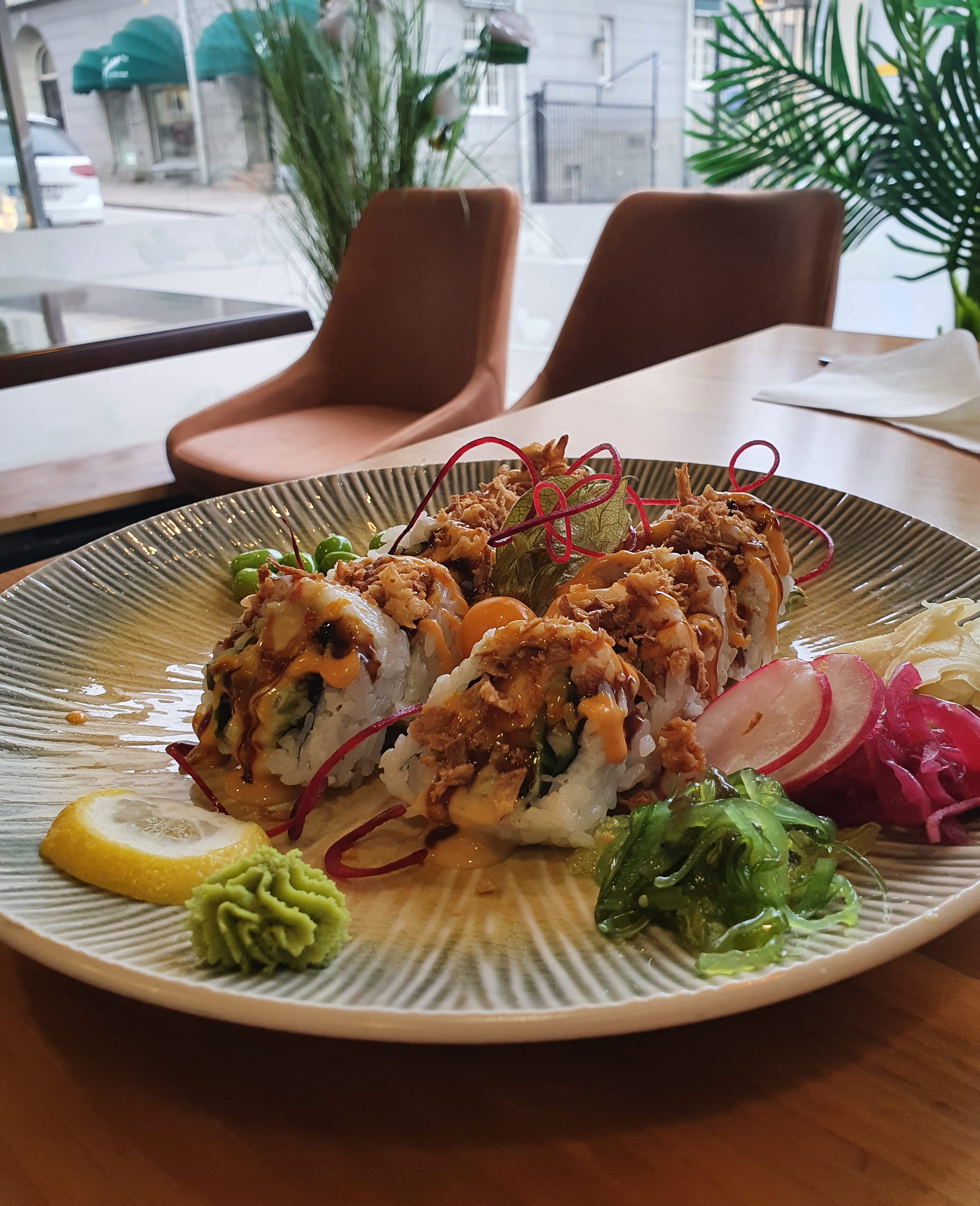 Tallrik med mat och grönsaker på ett bord med stolar och ett fönster med vy mot gata och hus i bakgrunden.