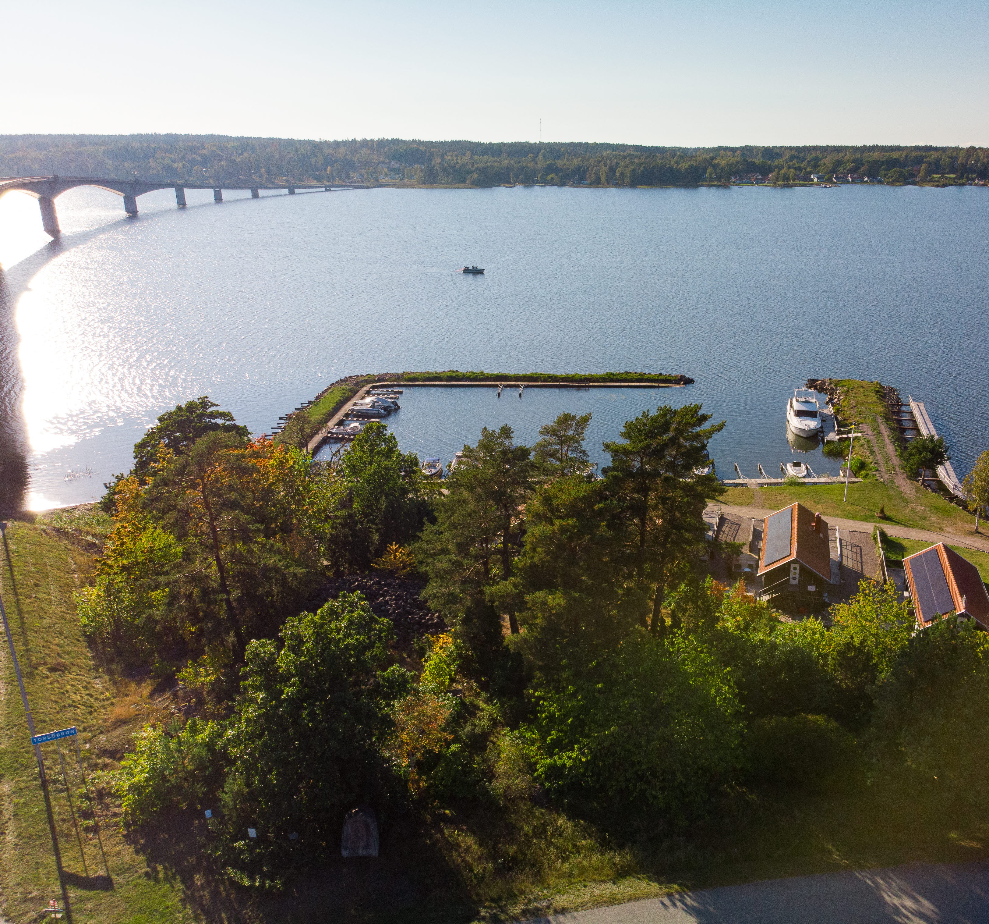 Flygfoto över vatten, träd, en bro och båtar i en hamn.