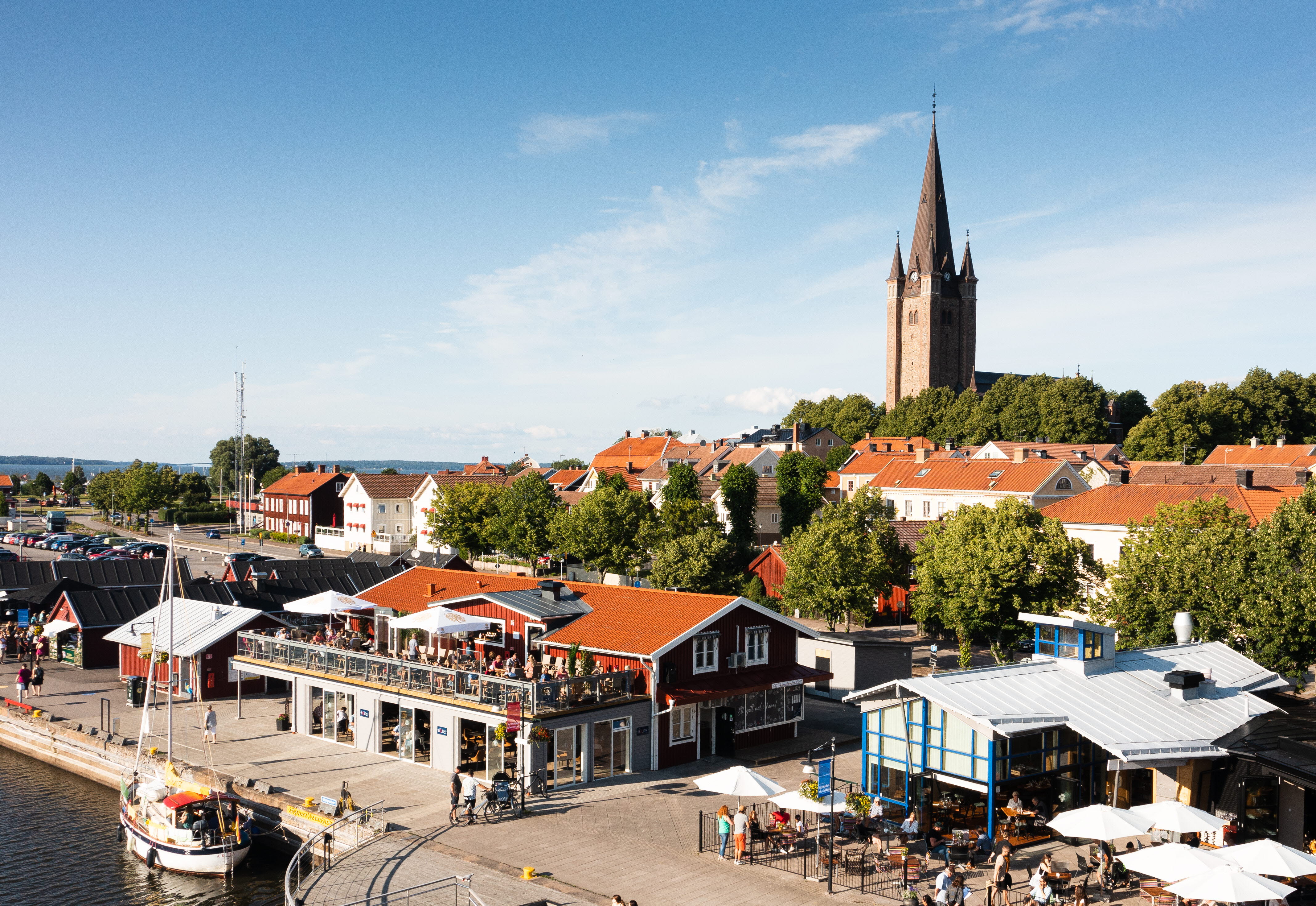 Flygfoto över Mariestads gästhamn med restauranger och bodar. I bakgrunden syns delar av Gamla Stan och Mariestads domkyrka.