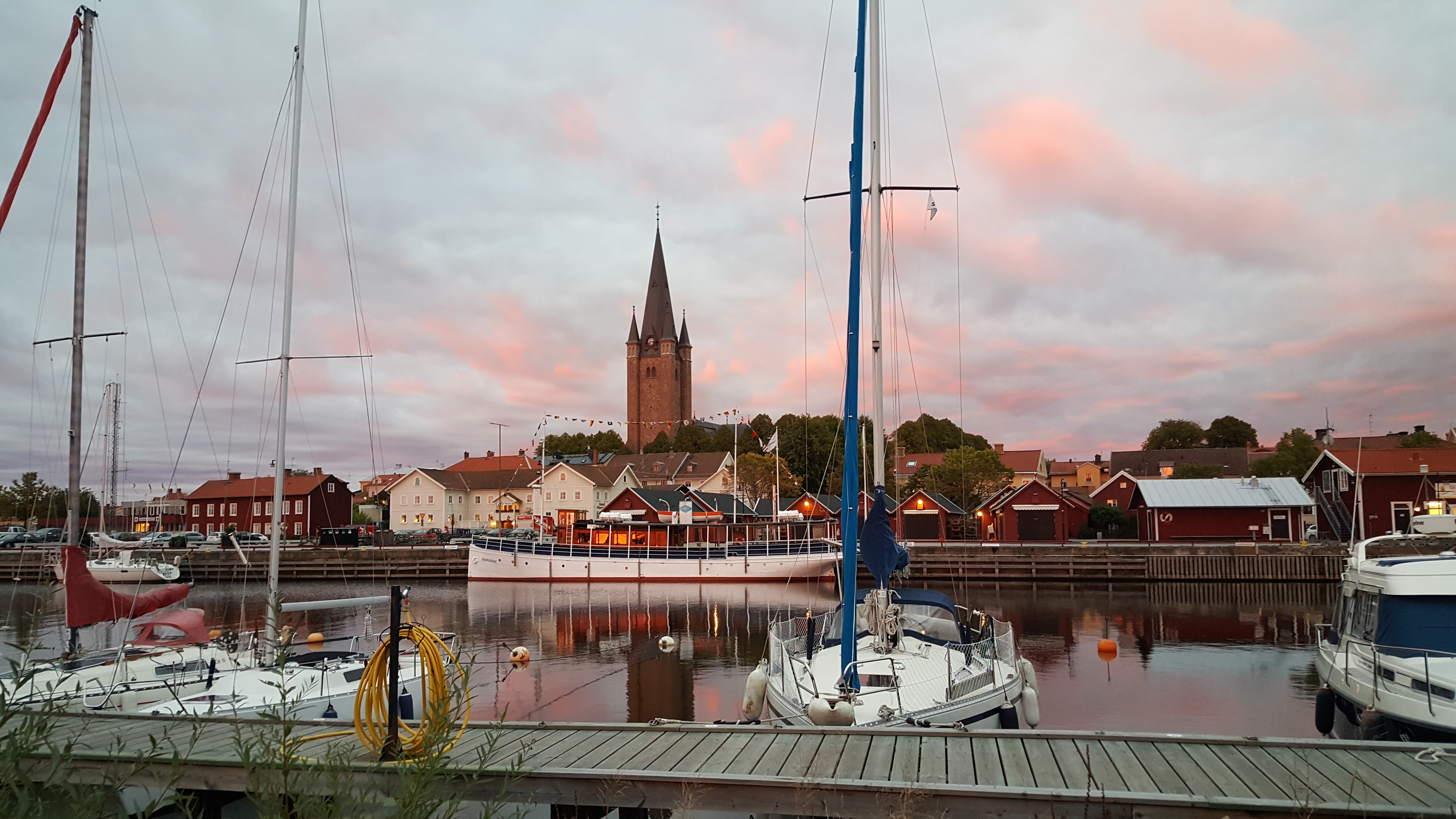 Skymning med enstaka båtar i hamnen i Mariestad med Gamla Stan och domkyrkan i bakgrunden.
