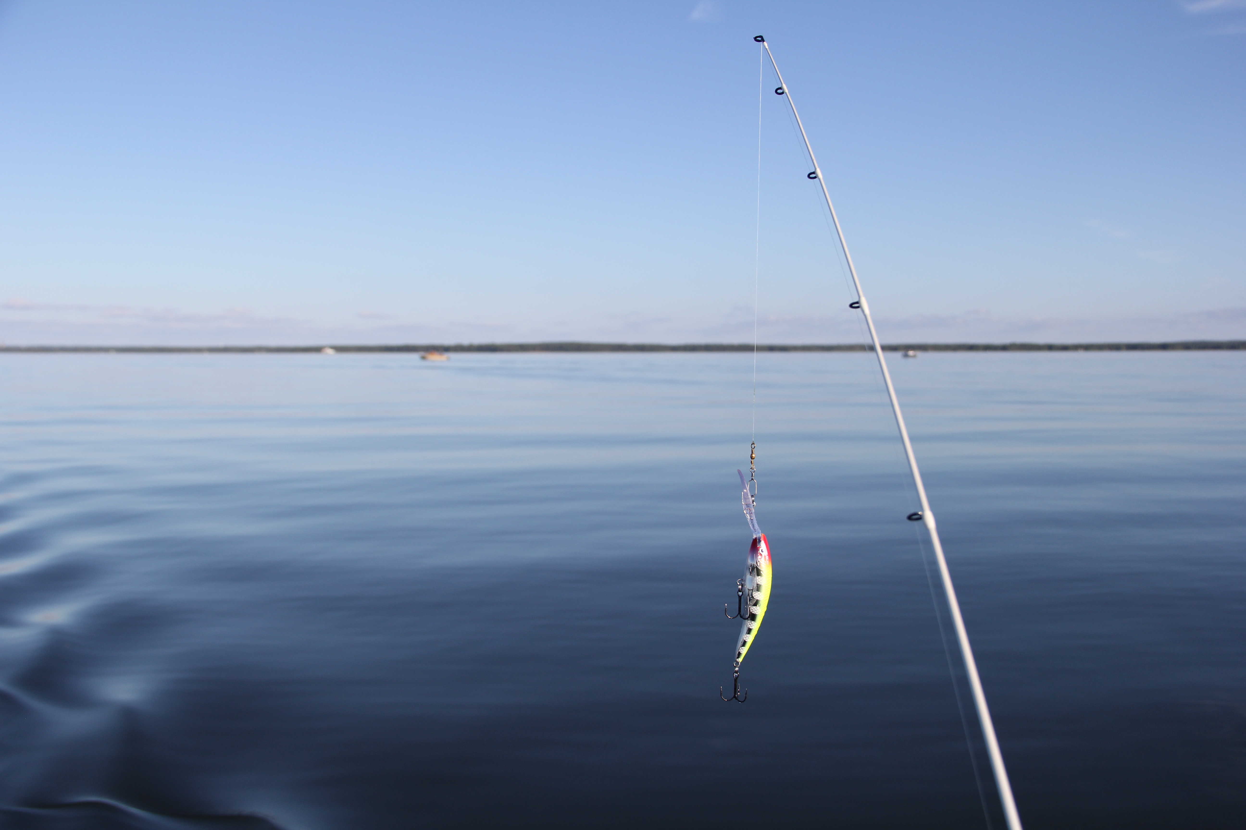 Fiskespö med drag i förgrunden. Vänern med två båtar i bakgrunden.