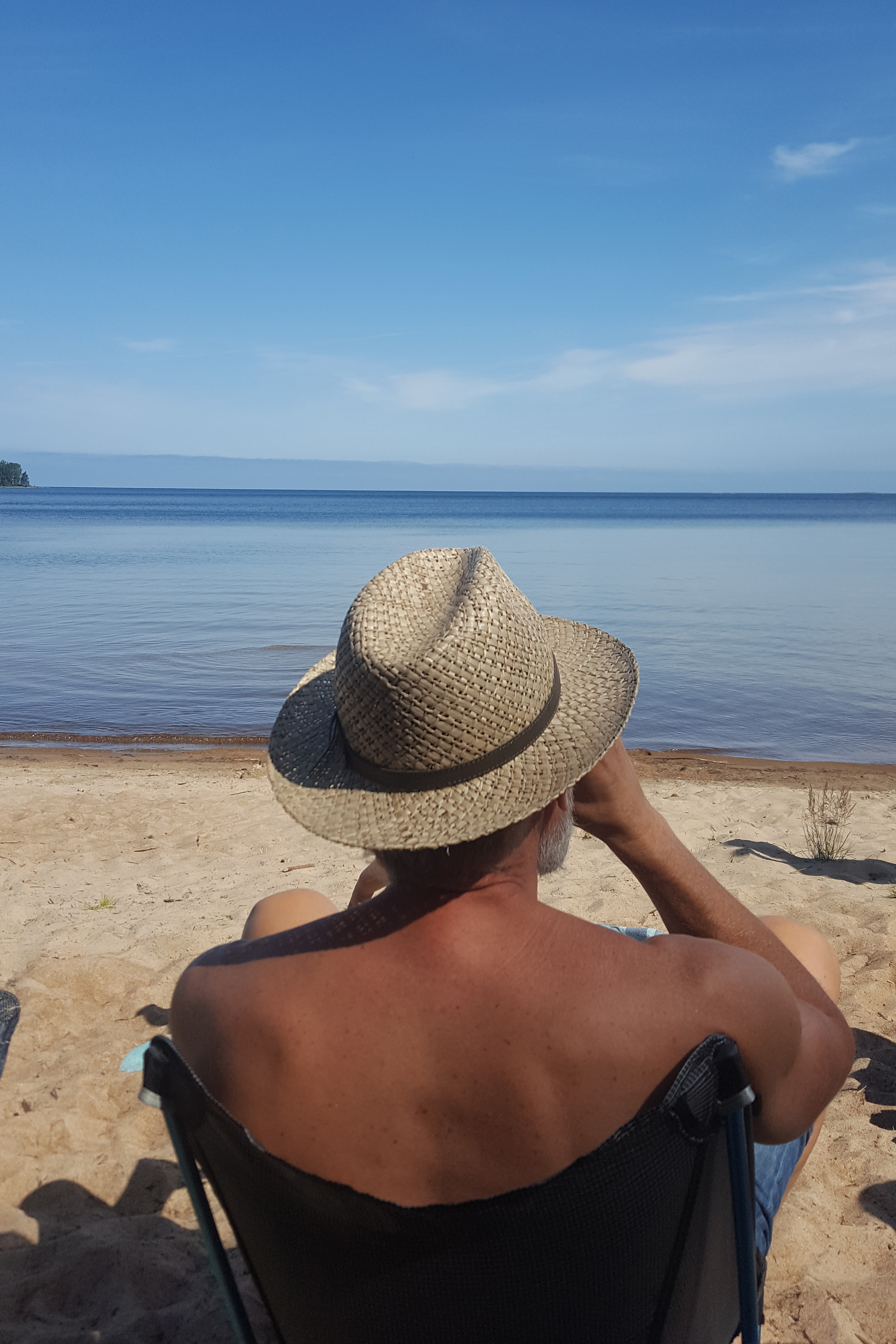 Man i hatt sitter i solstol och dricker kaffe på badstranden Store Vite Sand på Brommö i Vänern. 