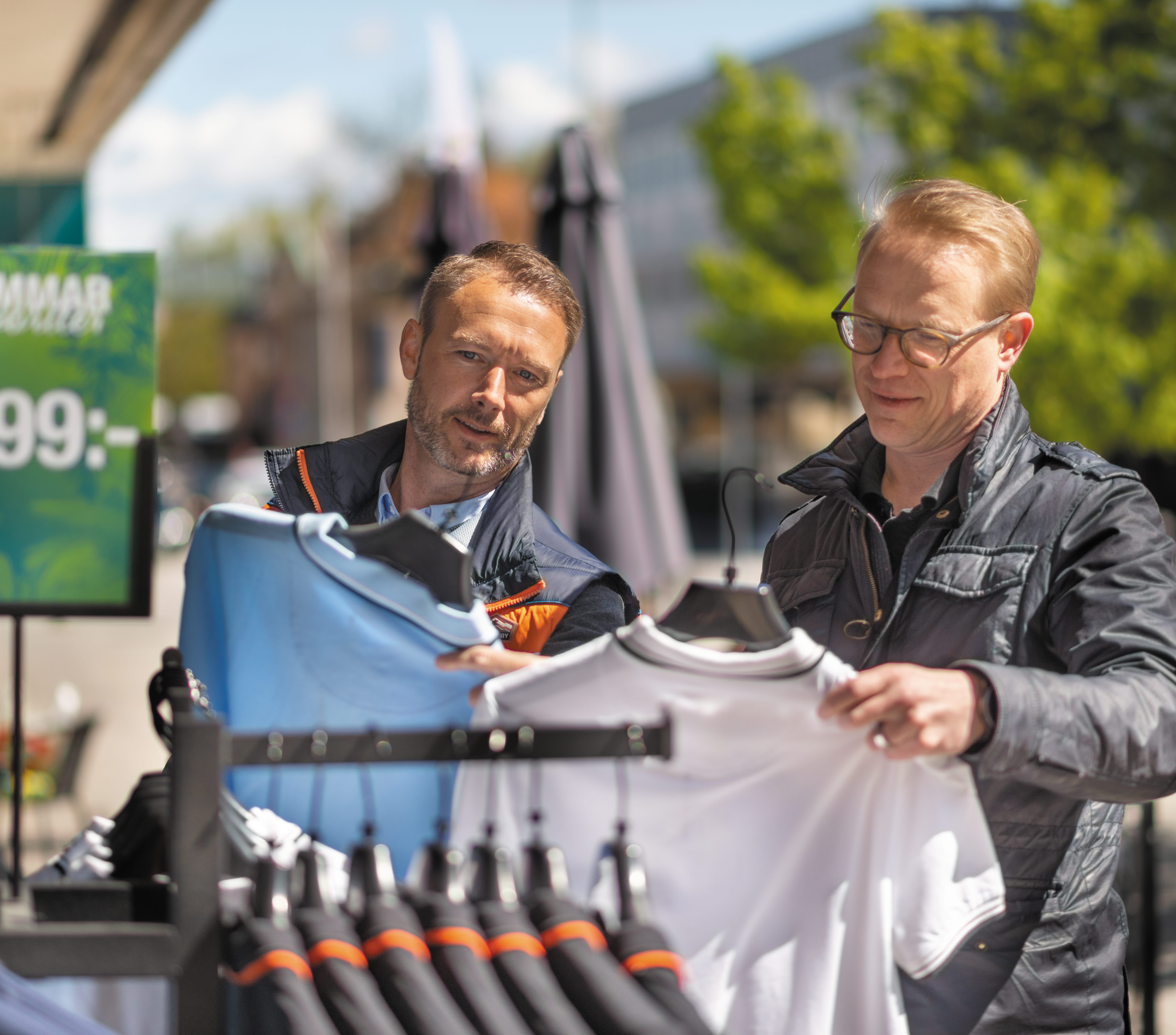 Two men looking at clothes hanging on racks outside the store.