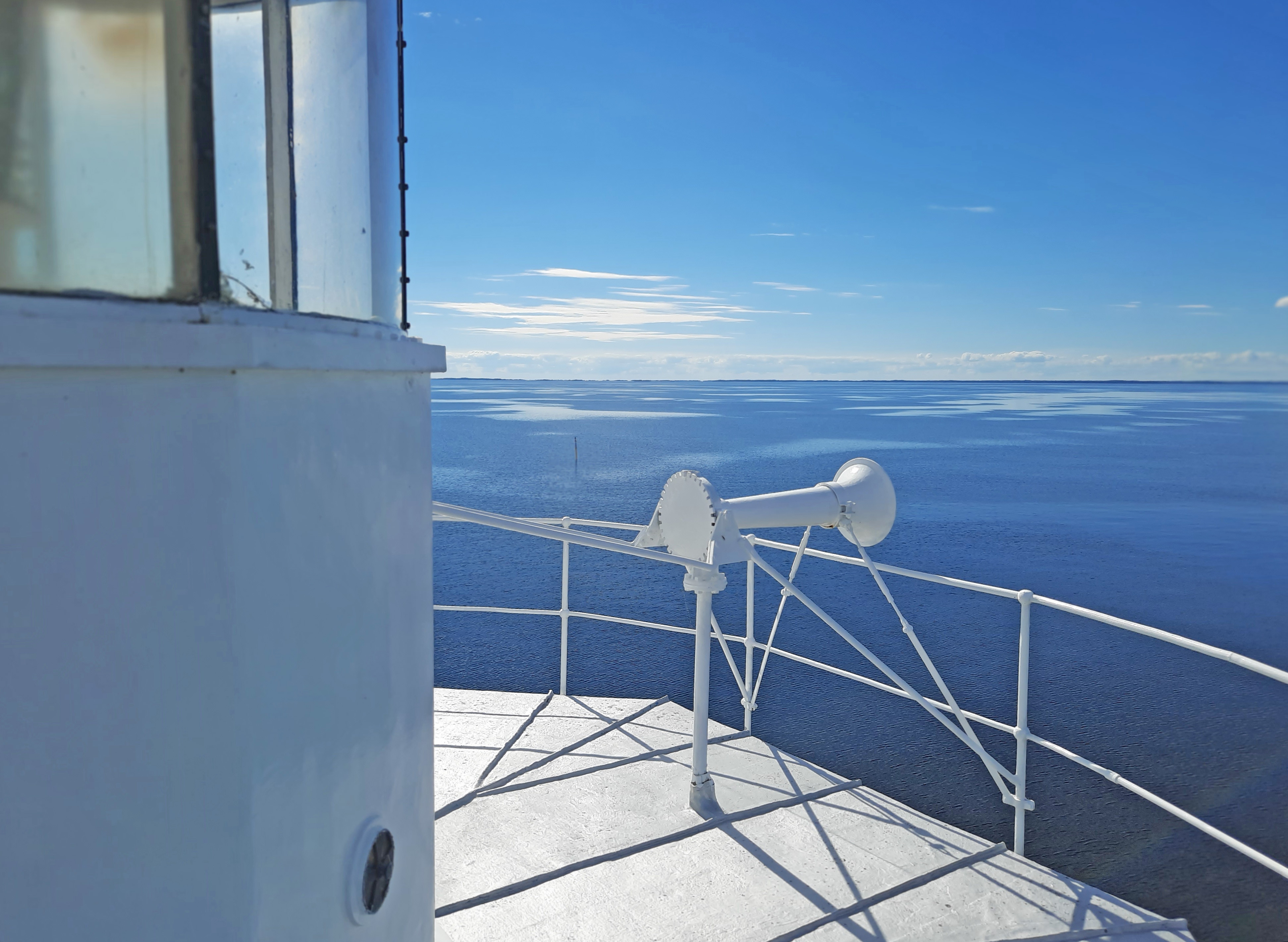 Utsikt från toppen av fyr med mistlur vid räcket och Vänern och horisonten i fonden.