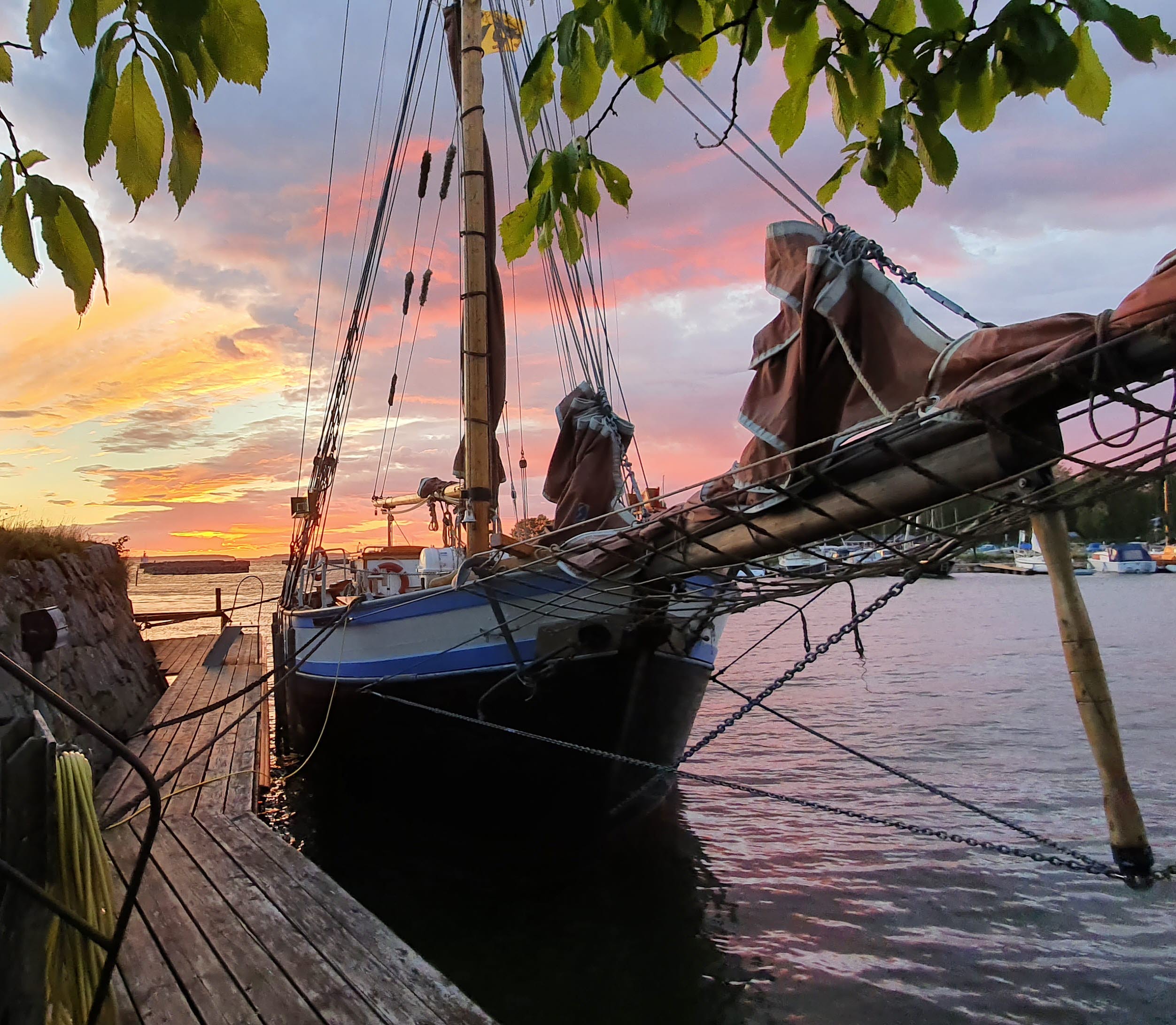 Vänerslupen Oskar 2:a ligger vid bryggan i solnedgången med fyren i Sjötorp i bakgrunden.