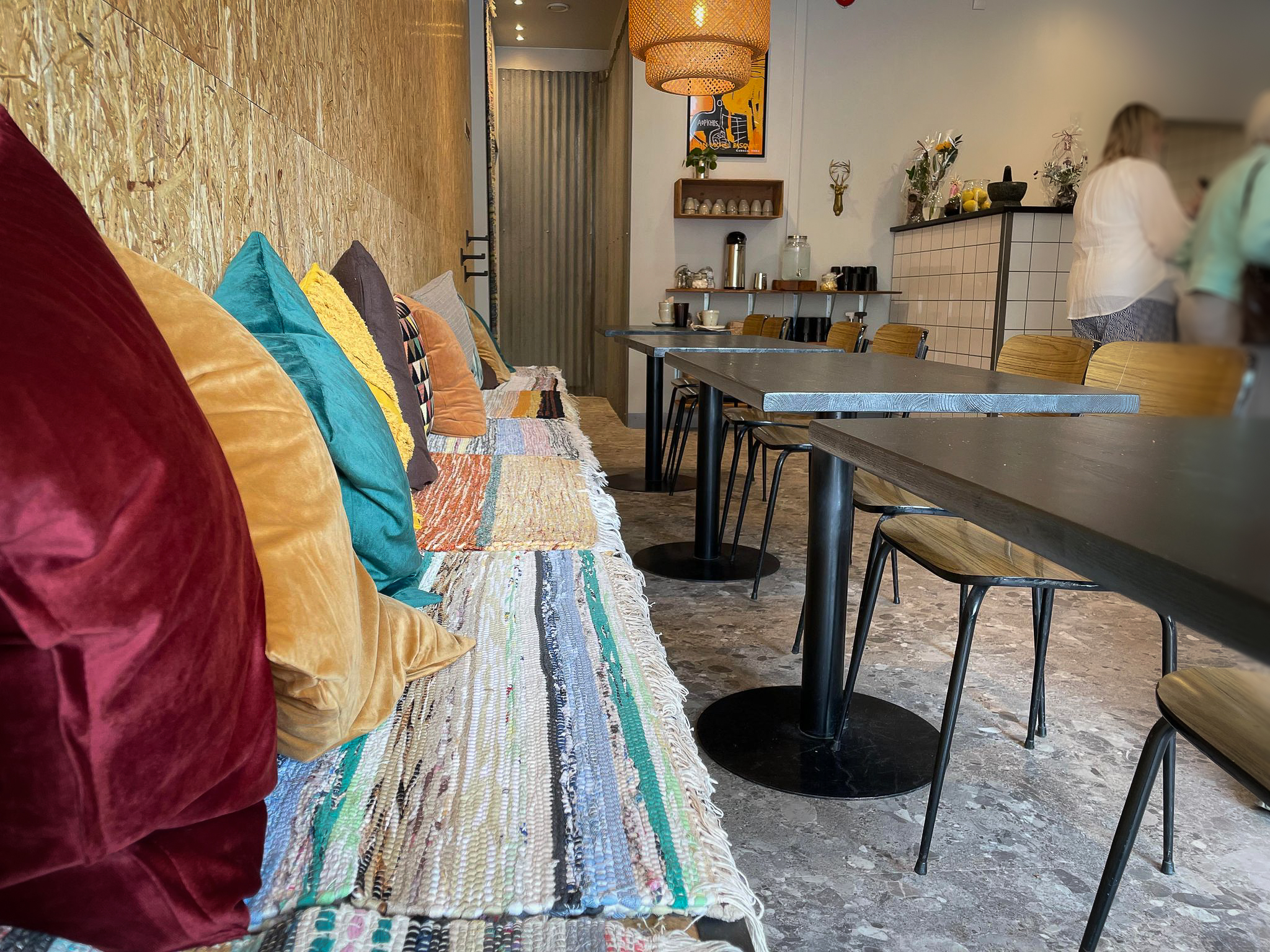 Bänk med färgglada trasmattor och kuddar och bord i restaurangmiljö.