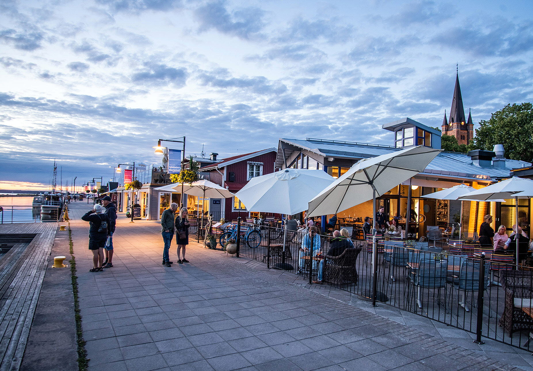 Skymning i gästhamnen med uteserveringen till restaurang Sill och Dynamit. Kyrktorn i bakgrunden.