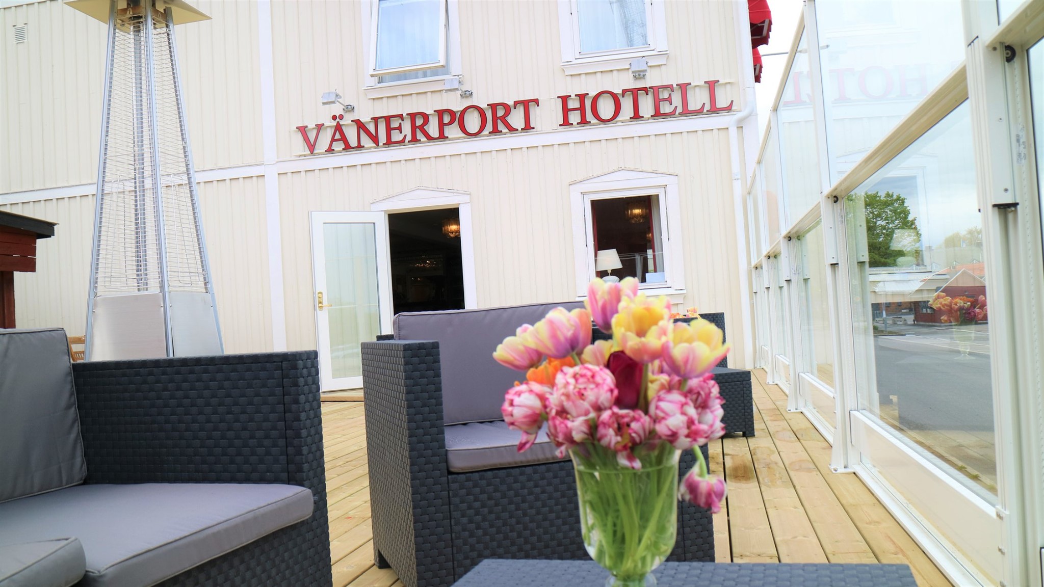 Hotell Vänerports terrass som vetter mot Hamngatan i Mariestad. Terrassmöbler och en blombukett i förgrunden, hotellfasad i bakgrunden.