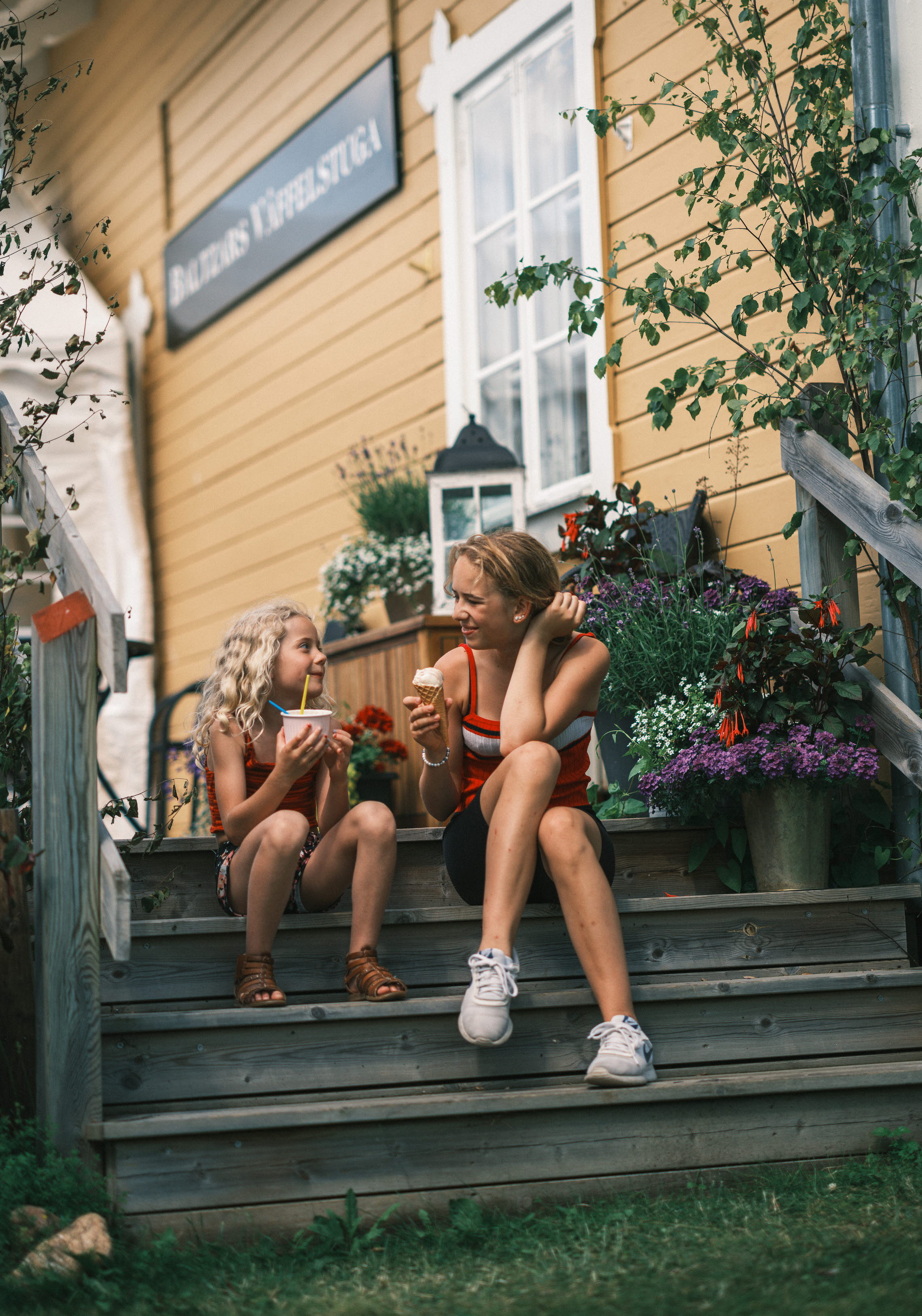 Två flickor sitter på trappan vid Våffelstugan i Sjötorp.