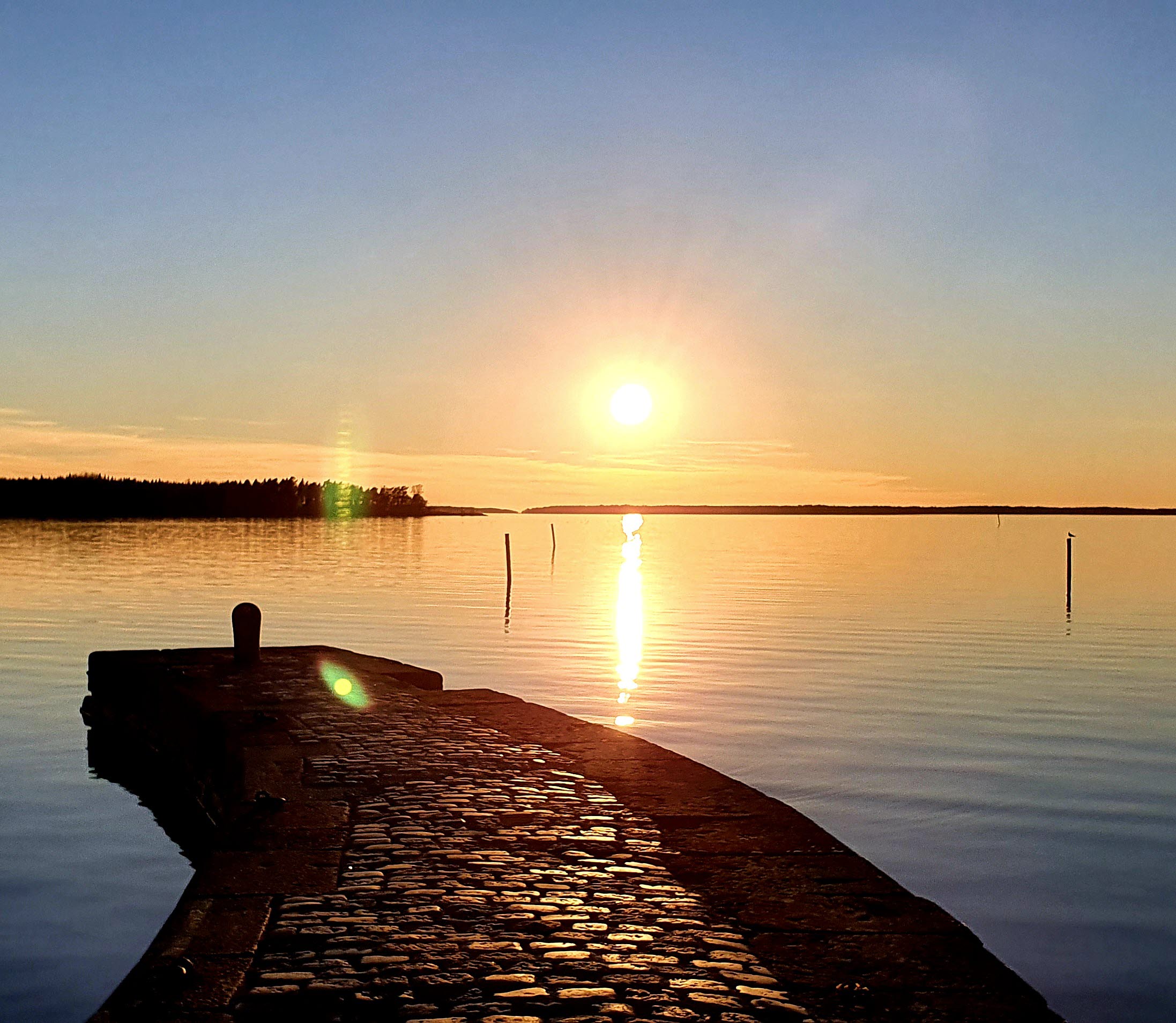 Stenlagd vågbrytare i Vänern med solen på väg ner i horisonten.