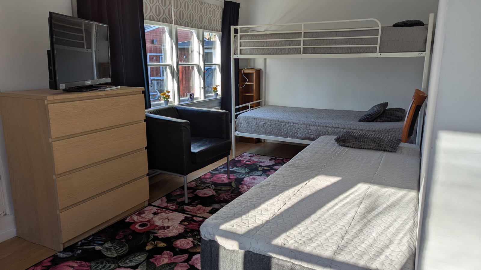 Rum med en våningssäng, en enkelsäng, en fåtölj och en byrå med en tv på.