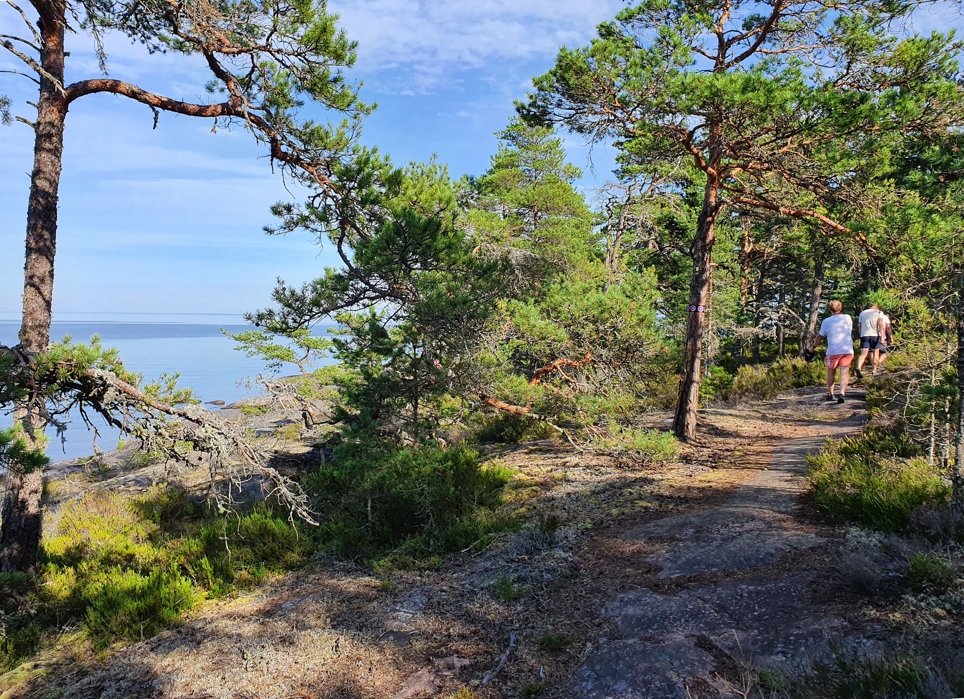 Tre personer vandrar på en stig bredvid vatten.