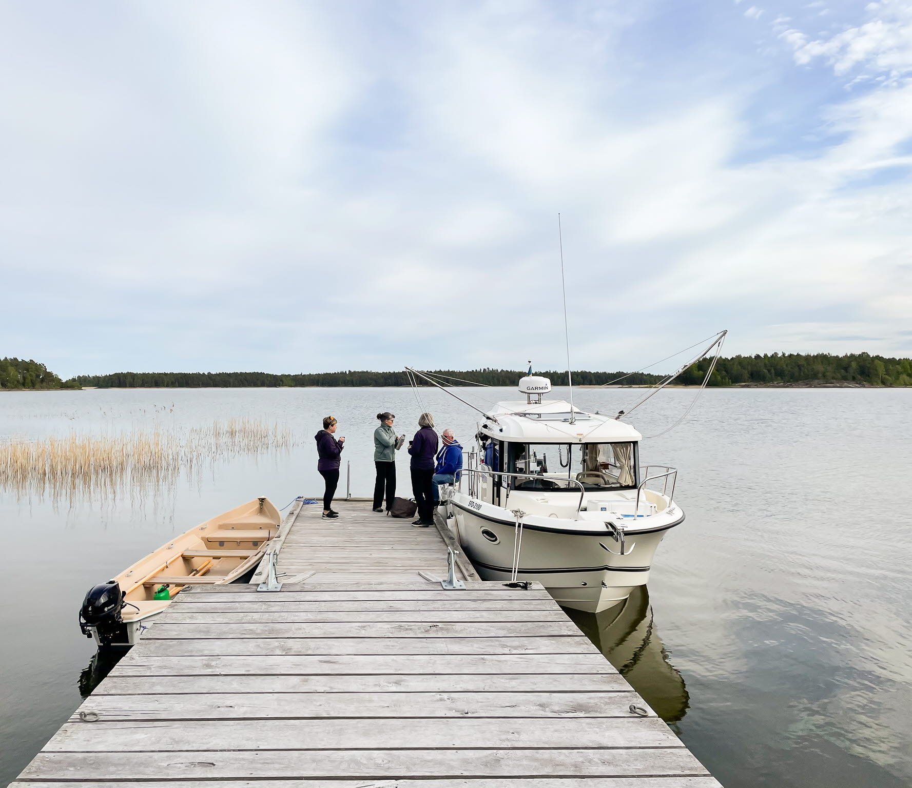 Vänertrollings båt ligger vid en brygga. Fyra personer står på byggan vid båten.