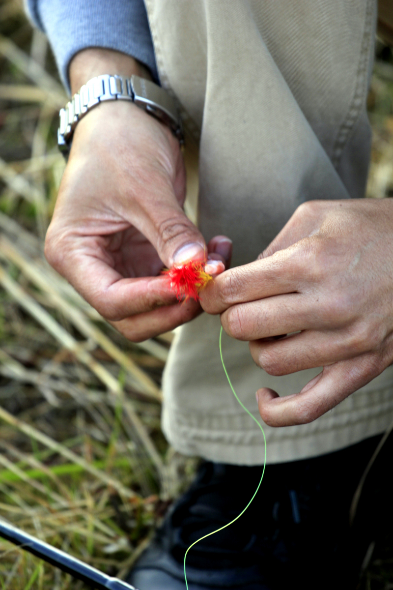 En bild på två händer som sätter en fiskekrok tillrätta på en fiskelina.