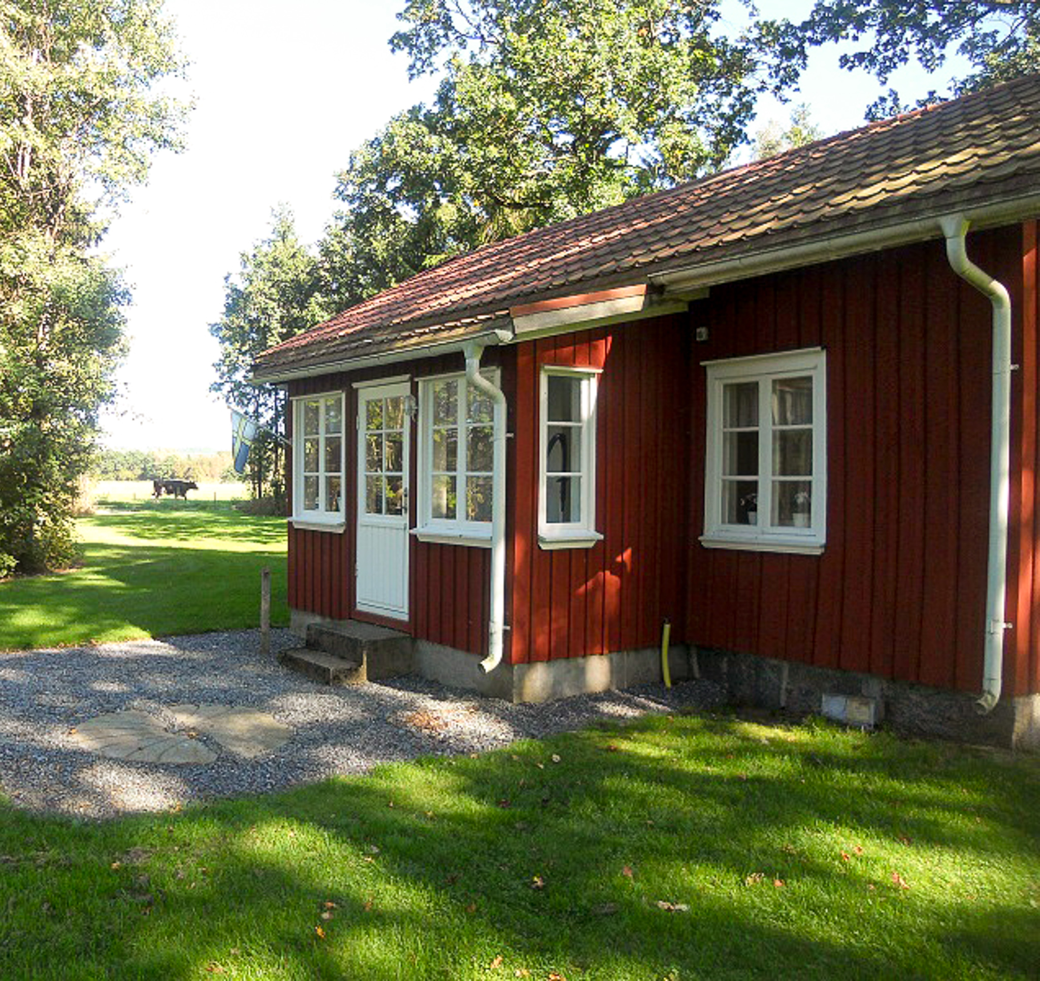 En närbild på ett rödmålat torp med vita spröjsade fönster. Huset är omgivet av grönska.