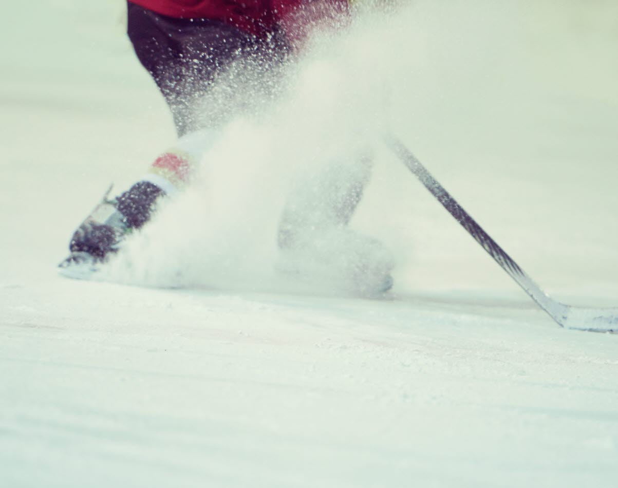 En bild på underkroppen av en person på is som bromsar med skridskorna så att det skvätter is