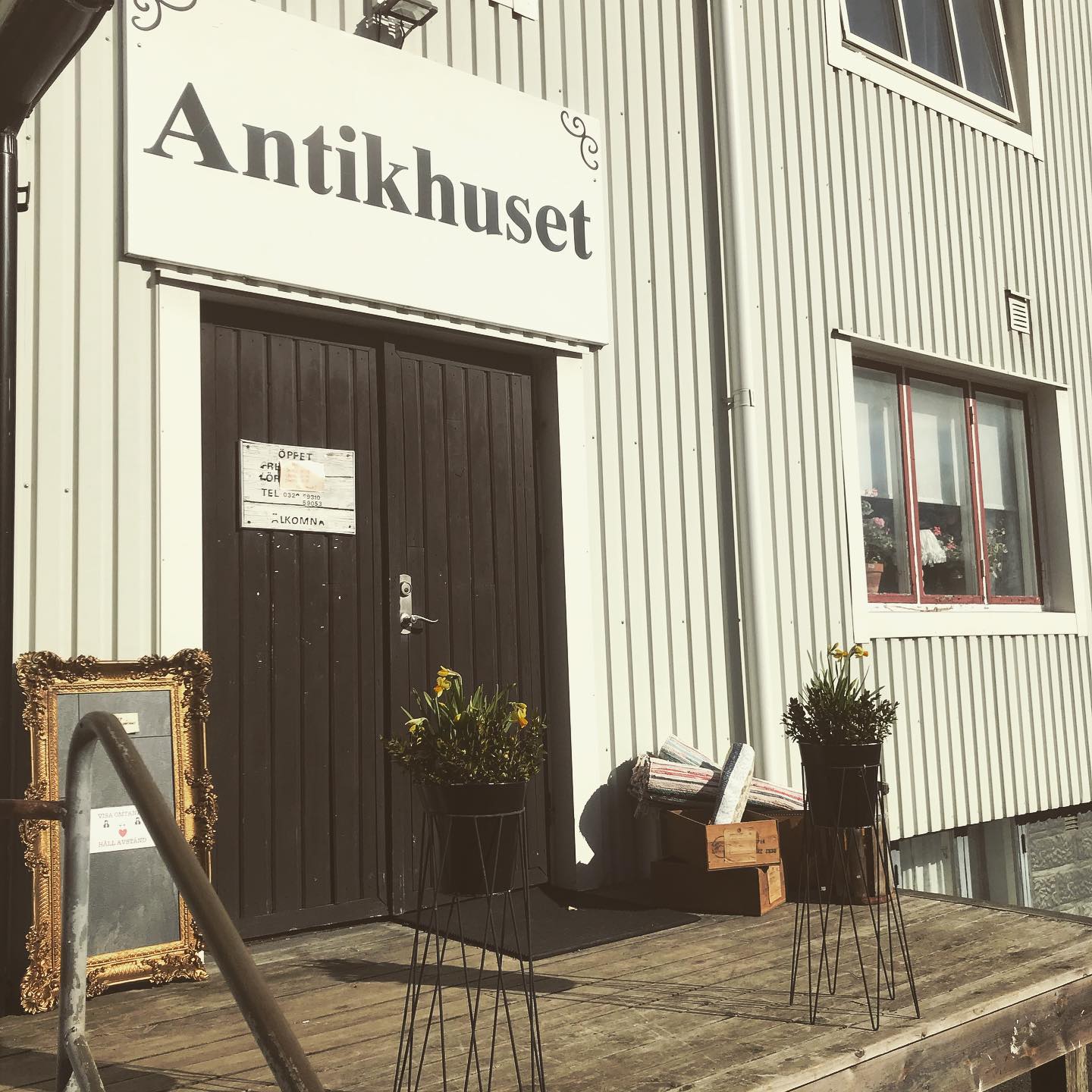 En bild på två svartmålade dörrar på en ljusgrå husfasad. Ovanför dörren sitter en skylt där det står "Antikhuset".