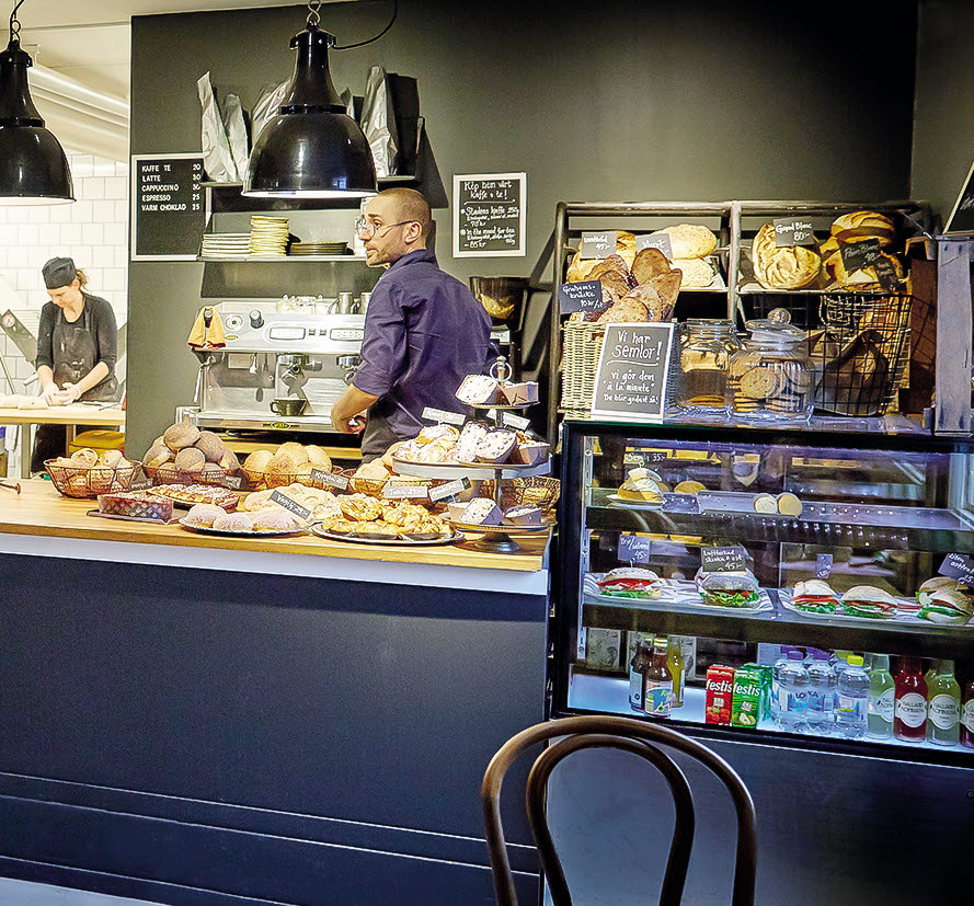 En bild från insidan på ett café där det står mängder av kakor och bakverk på cafédisken.