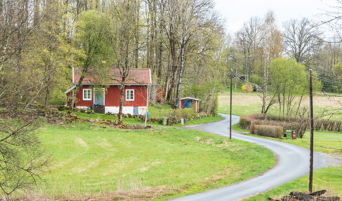 En slingrande väg genom grönt landskap. I bakgrunden syns ett rött hus.