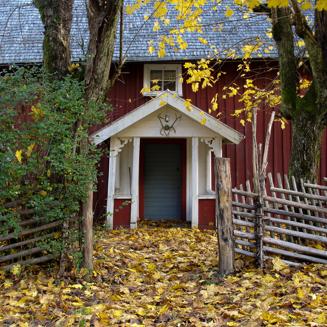 En bild på en veranda på ett gammalt torp. På marken ligger gula höstlöv.