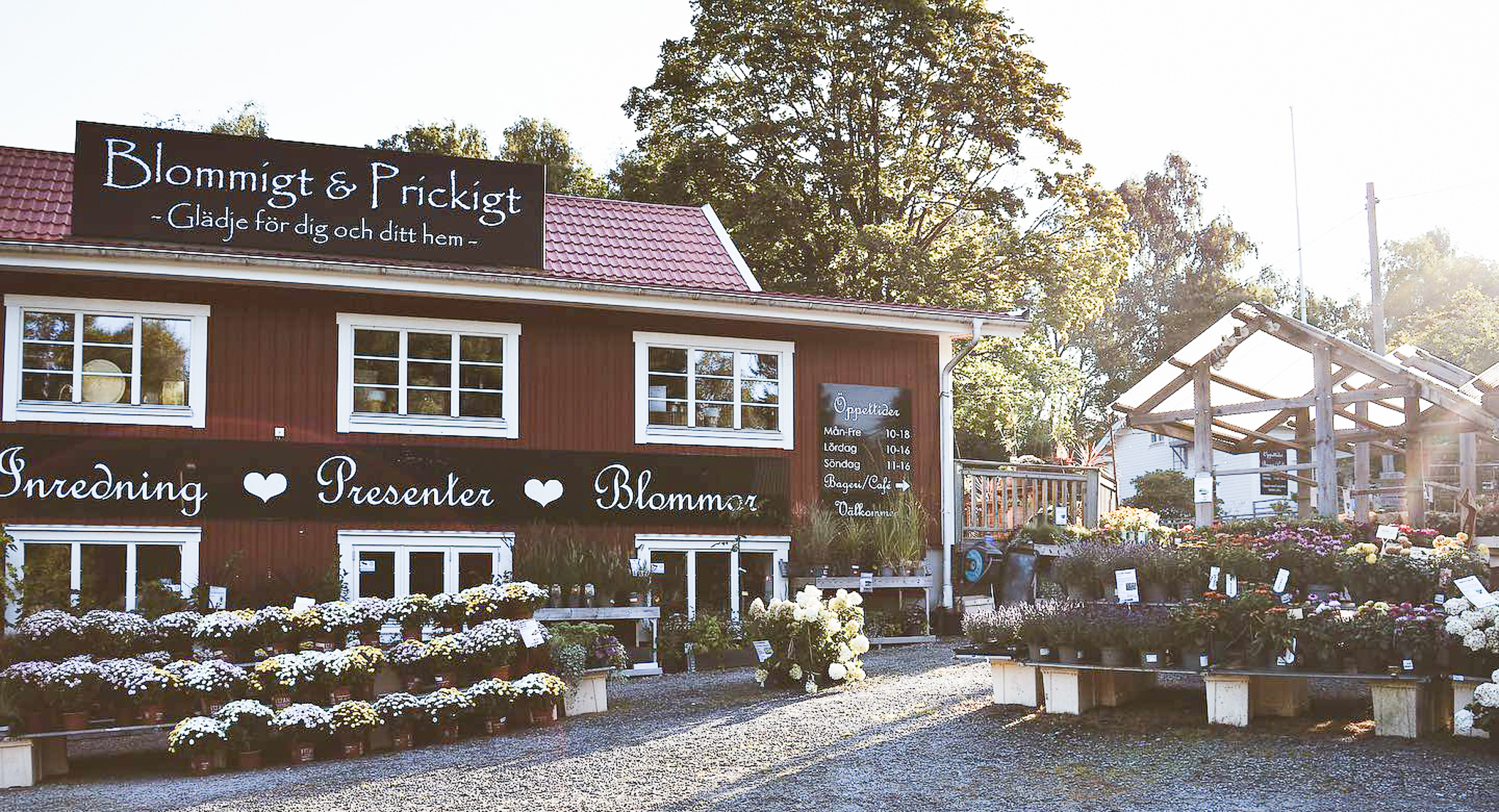 En bild på utsidan av en rödmålad butik med mängder av blommor och växter som står uppradade till försäljning.