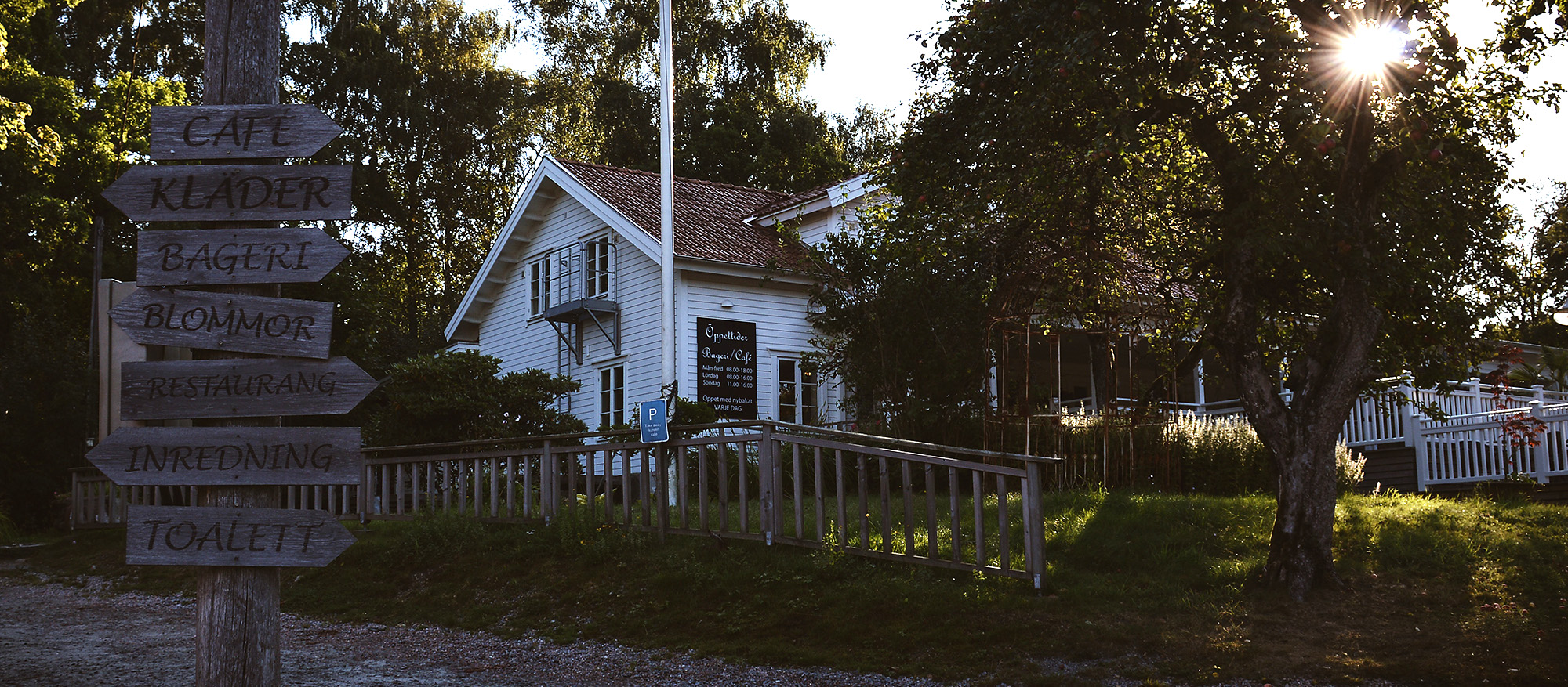 En bild på ett vitt hus omringat av grönska från träd, gräs och skog.