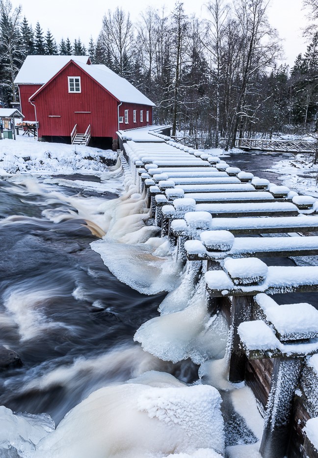 En bild på en rödmålad kvarn intill ett isigt vattendrag