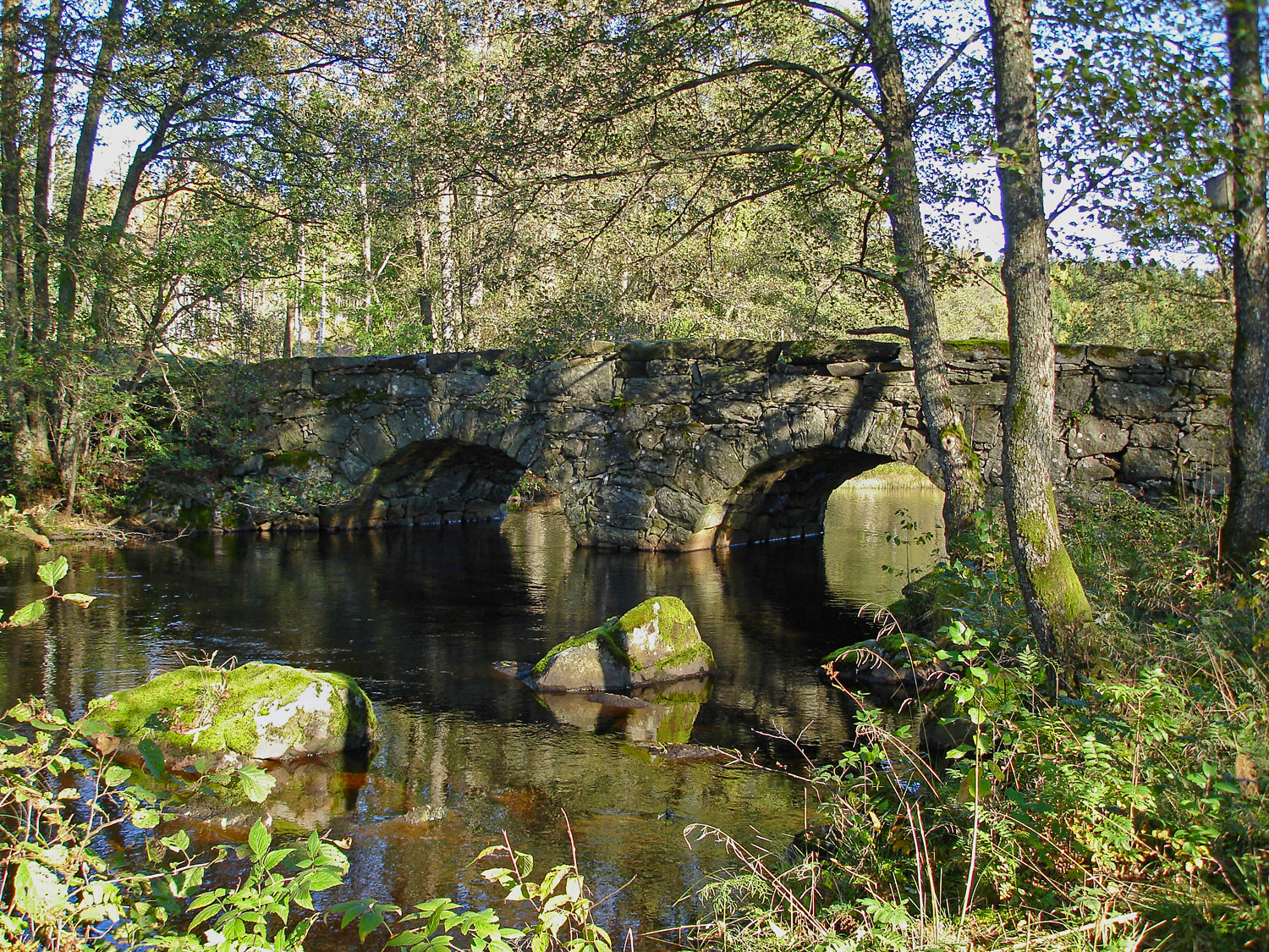 En gammal stenvalvsbro över stilla vattendrag