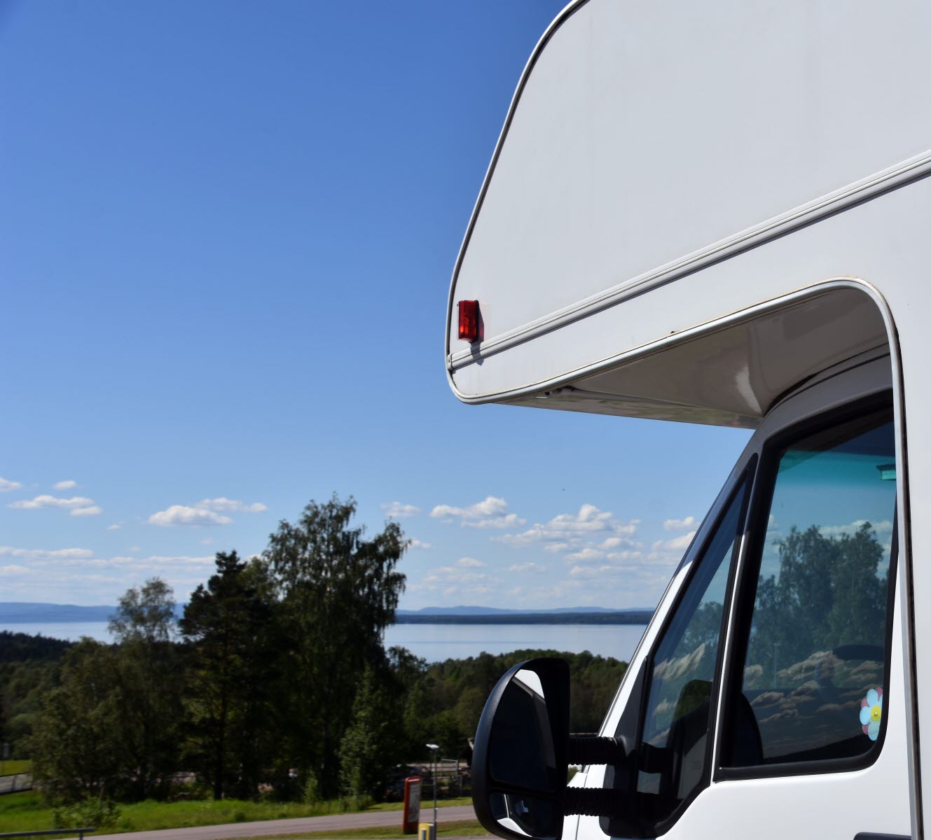 En närbild på nosen av en husbil. I bakgrunden kan man skymta en stor sjö.