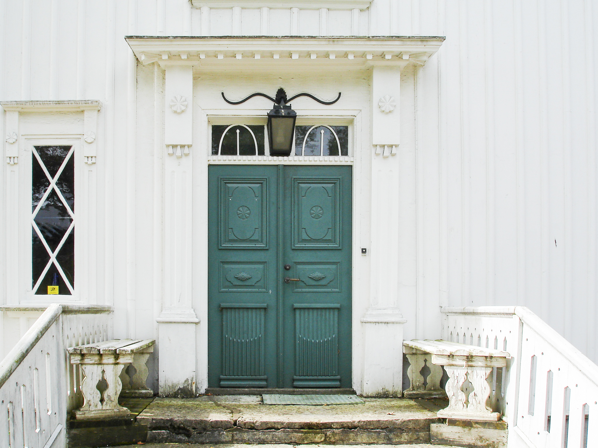 En närbild på en grön pardörr som sitter på ett vitt trähus.