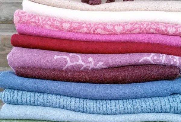 En bild på vikta tyger av ull som lagts i en hög. På toppen står en häst av tovad ull.