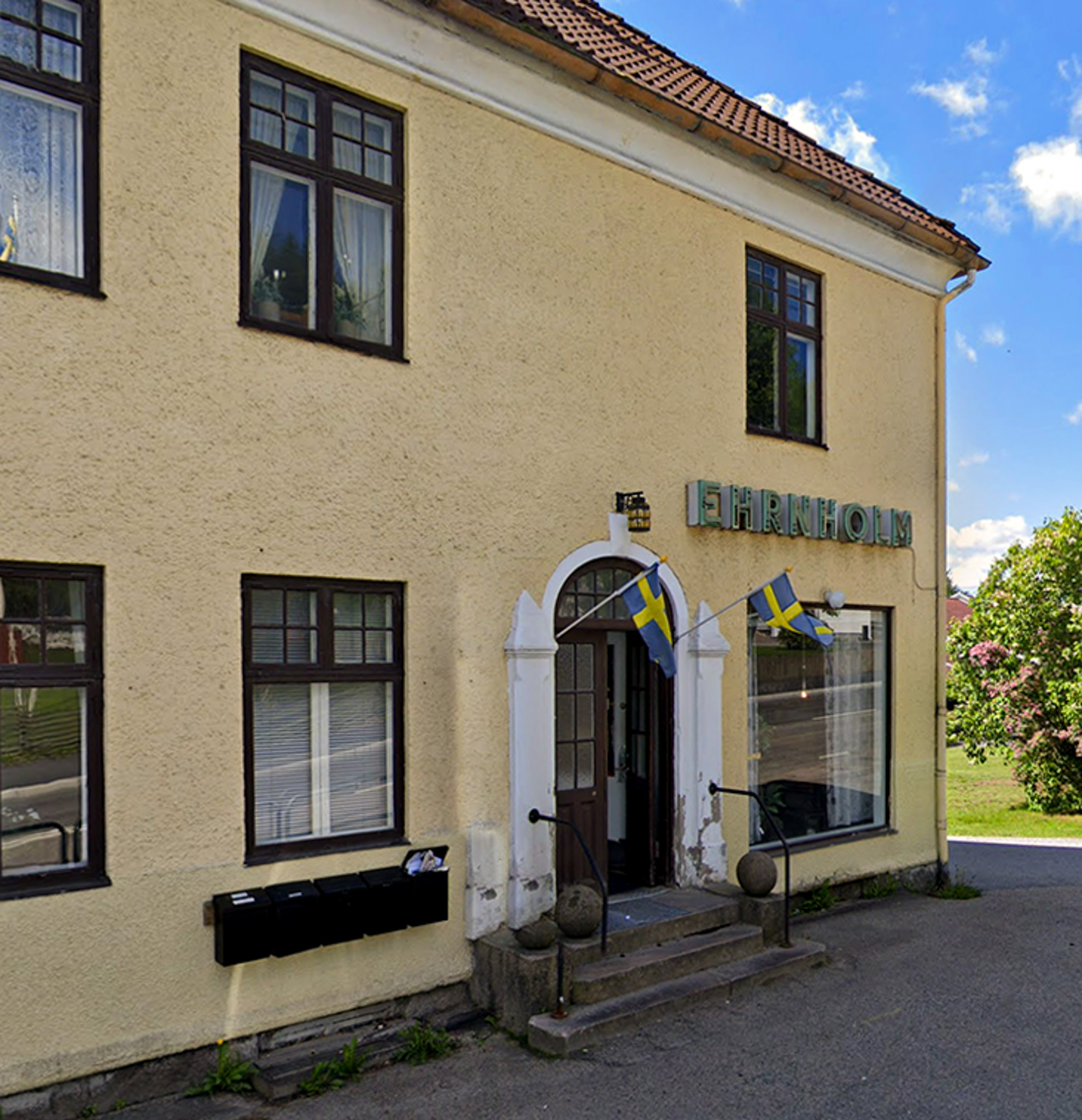 En bild på ett gult putsat hus med en vacker dörr som står öppen. På fasaden sitter en caféskylt.