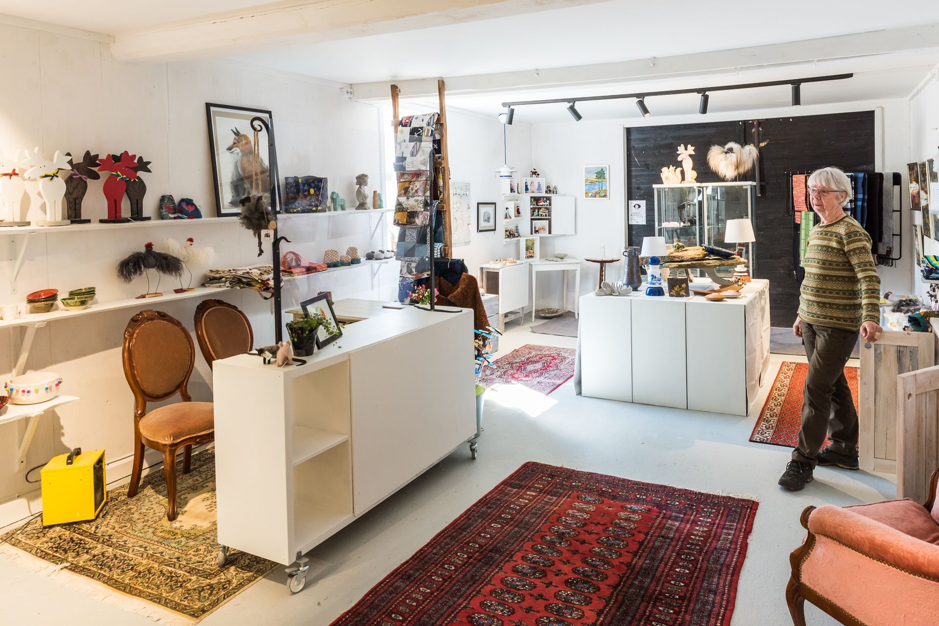 En bild inifrån en butik med hantverksföremål. Tak, väggar, golv och möbler går i vitt och gör att de orientaliska mattorna på golvet poppar - liksom alla varor som står uppradade på hyllor.
