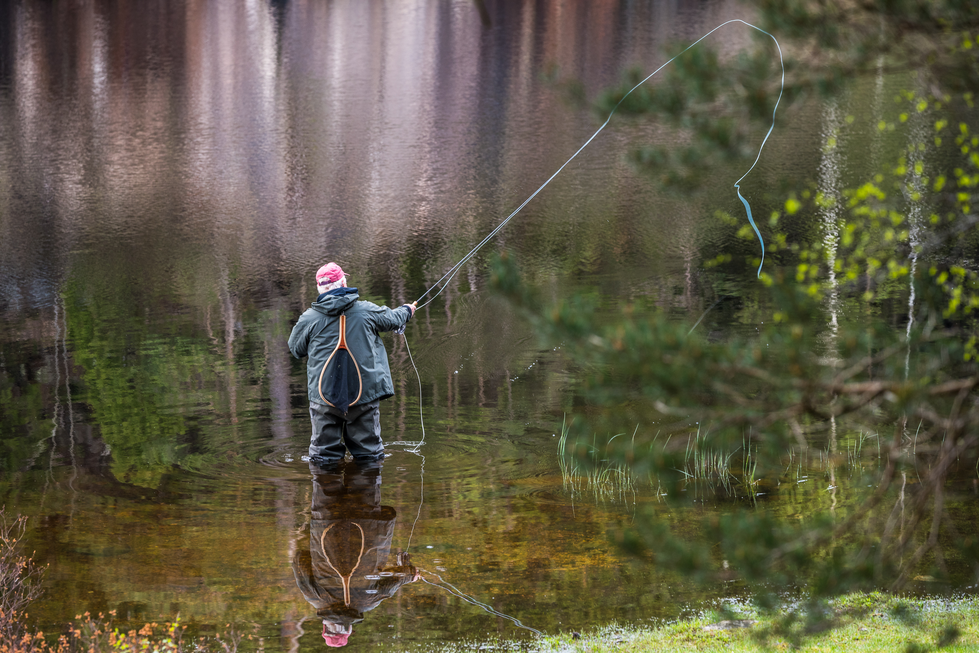 En person står i vattnet och fiskar i Stockasjöarna i Öxabäck. Det speglar sig i vattnet.