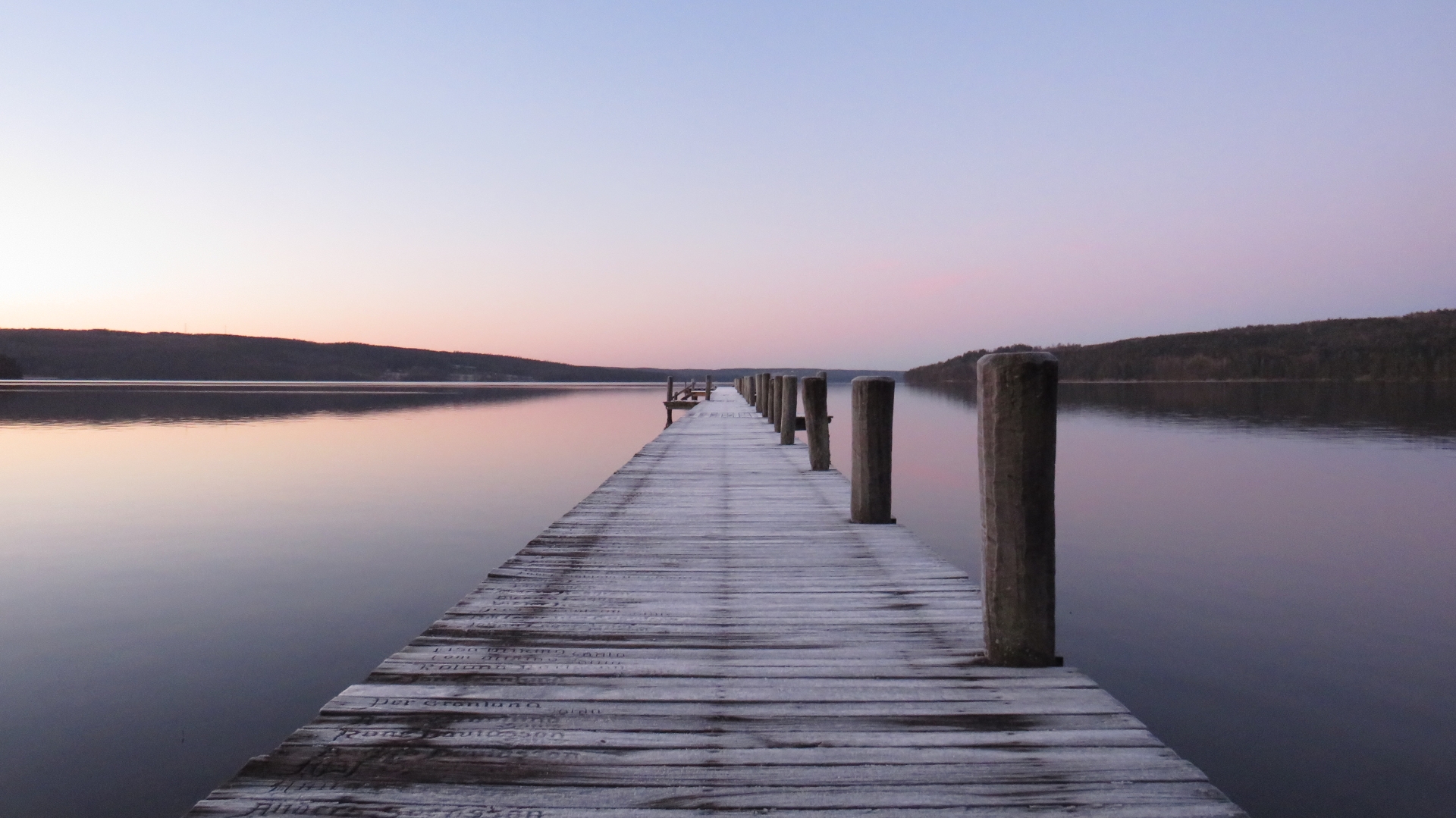 En bild på en frostig träbrygga som sträcker sig ut i en spegelblank sjö.