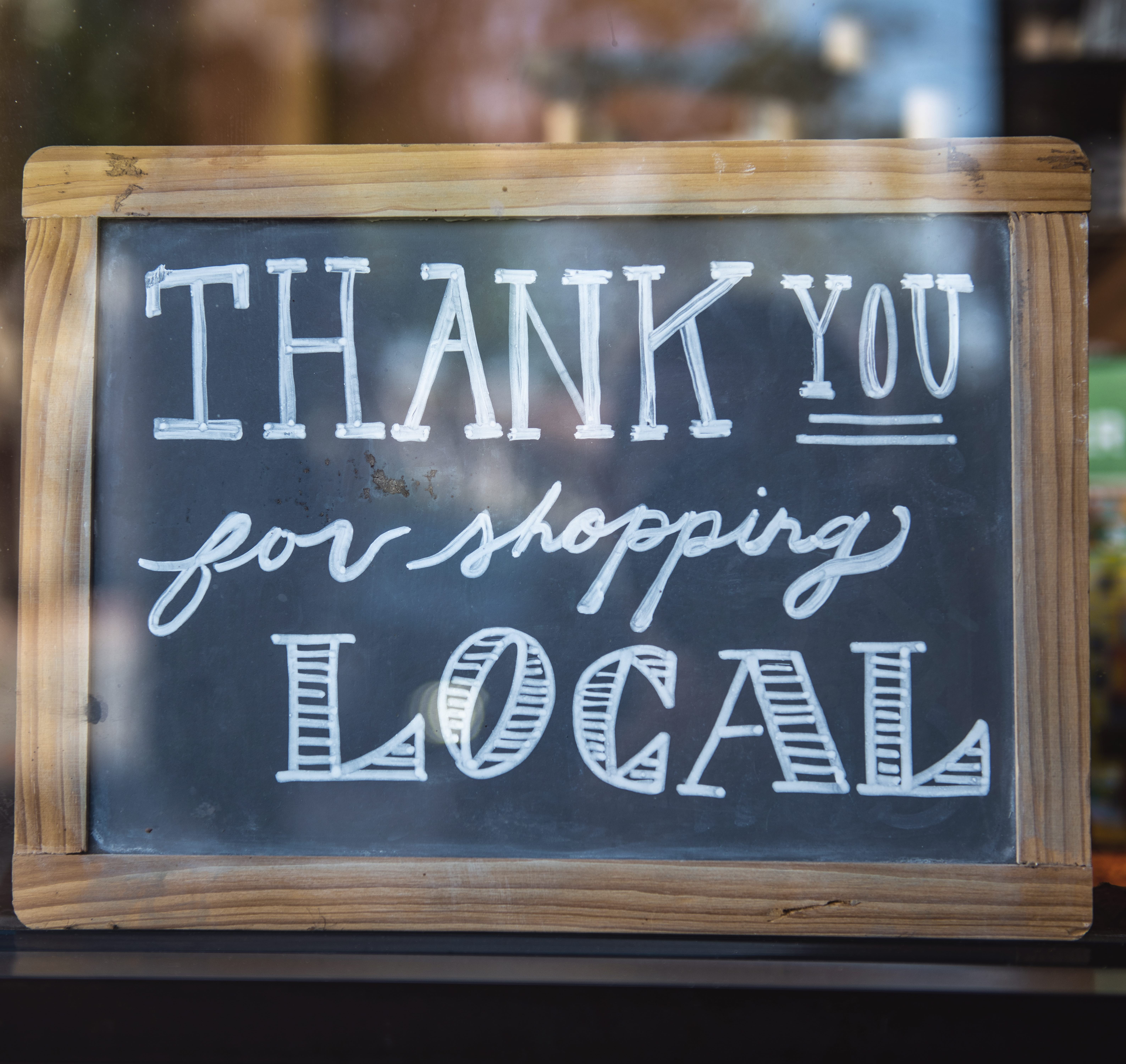 En bild på en skylt där det står "Thank you for shopping local".